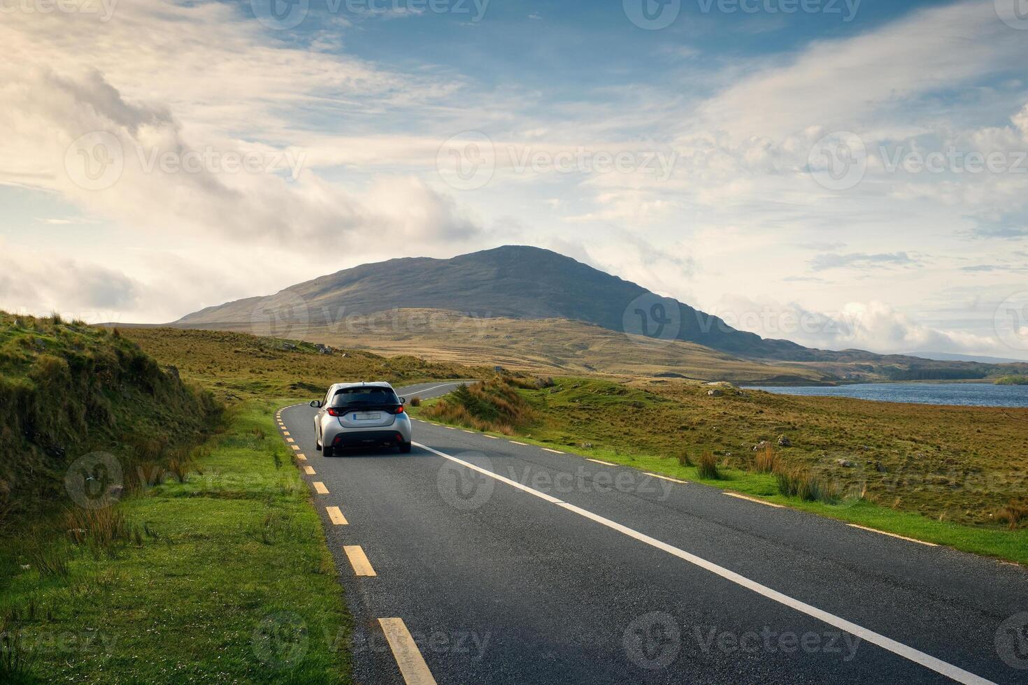 Car driving on empty scenic road trough nature by the lough inagh with mountains in the background at Connemara National park in county Galway, Ireland photo