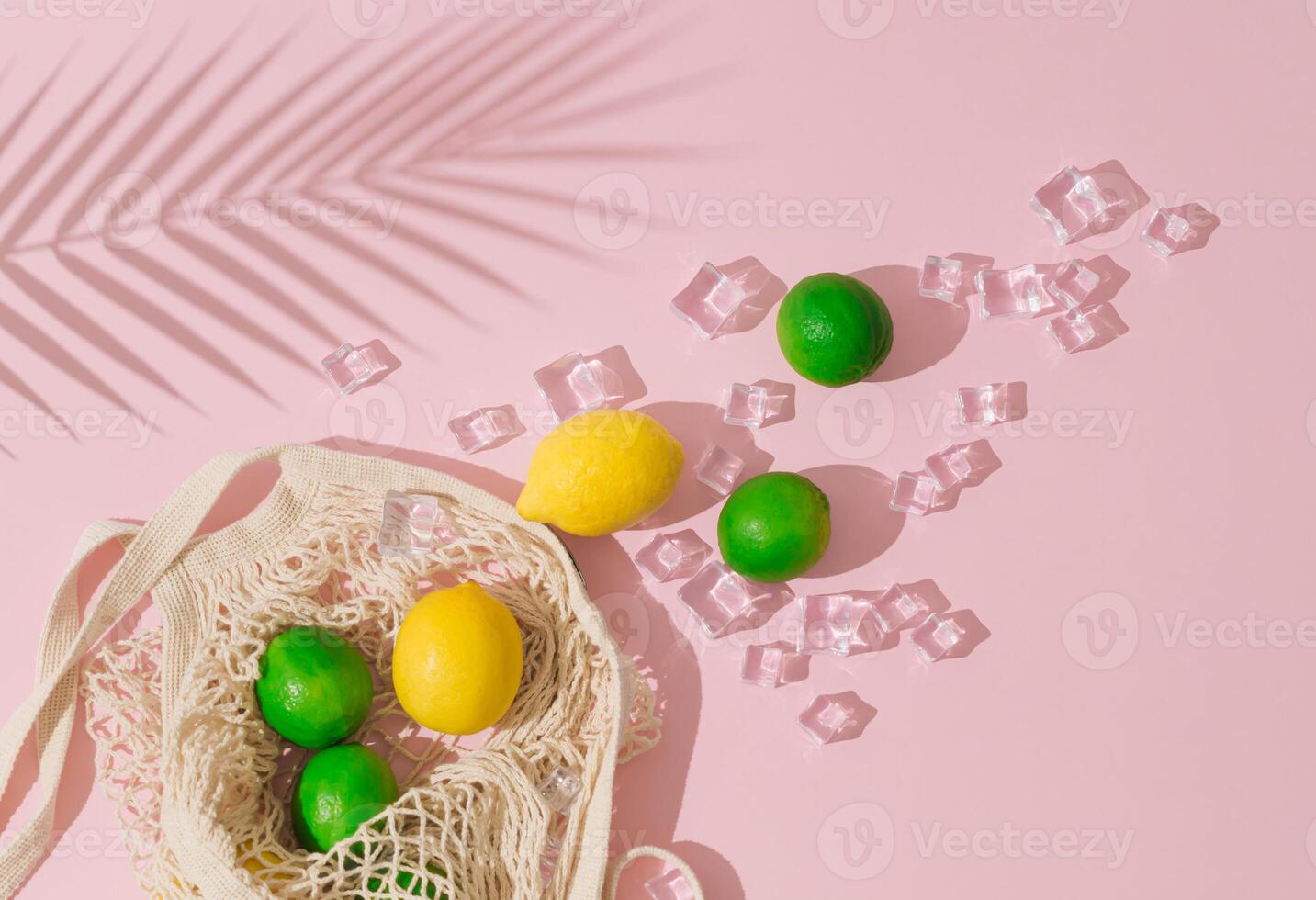 Summer sunlight scene made with crochet net shopping bag, lime, lemons, ice cubes and tropical palm tree leaf shadow on light pastel pink background. Minimal summer fruit concept. Flat lay. photo