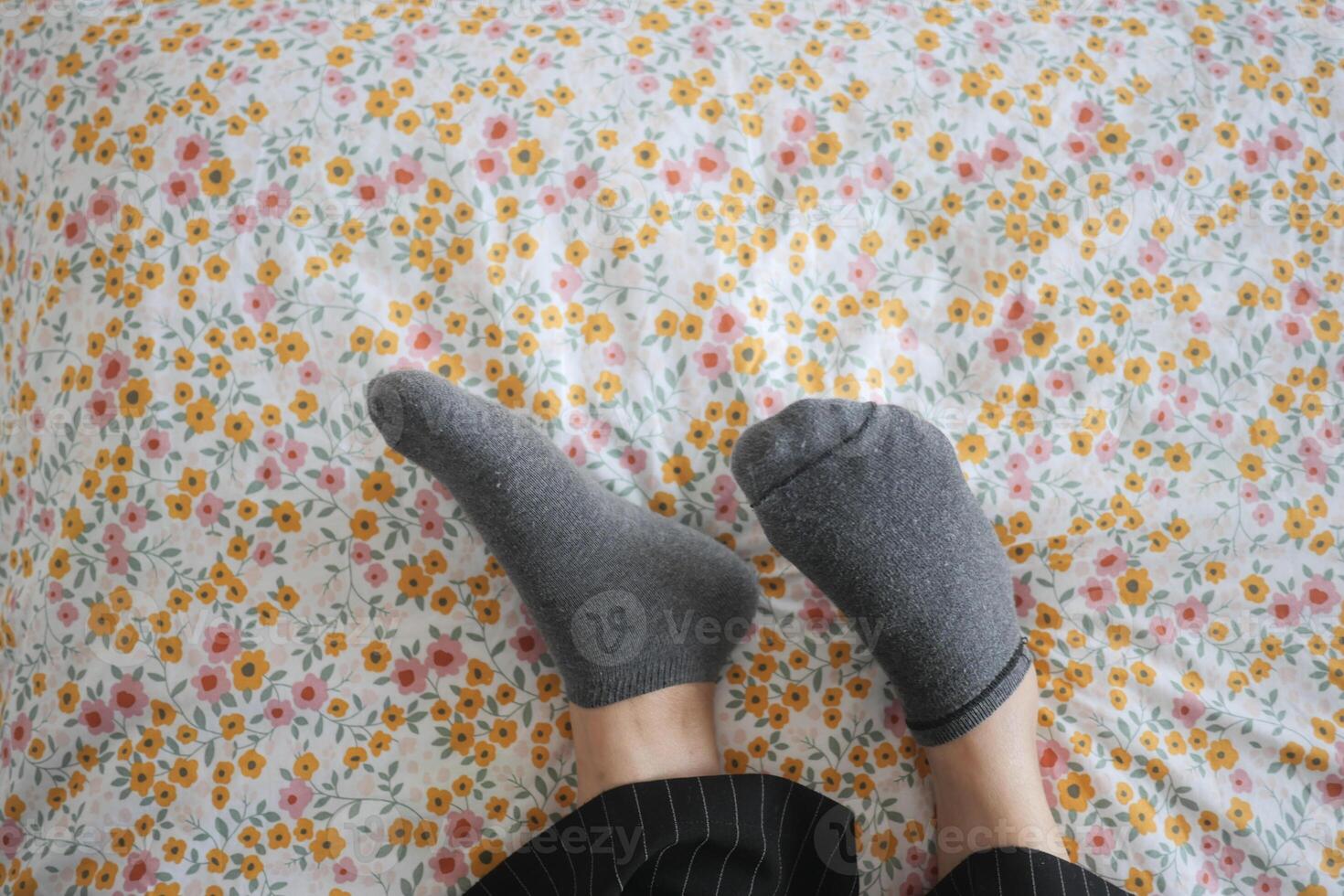 un mujer es tendido en un cama con su pies arriba y vistiendo calcetines foto