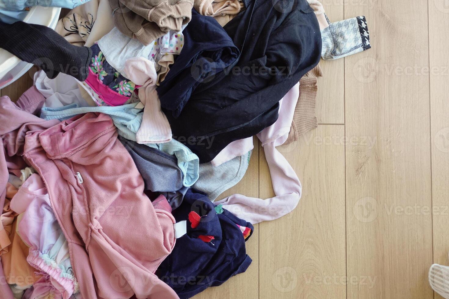 Clothes pile next to laundry basket filled with garments, on hardwood floor photo