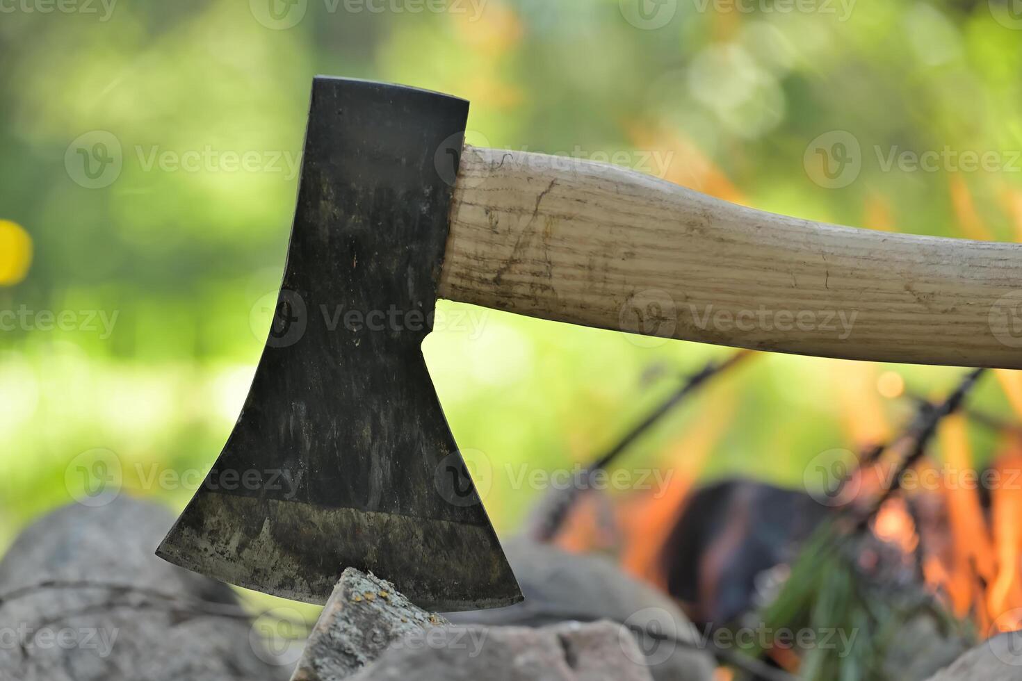 Hatchet embedded in a log of wood opposite campfire photo