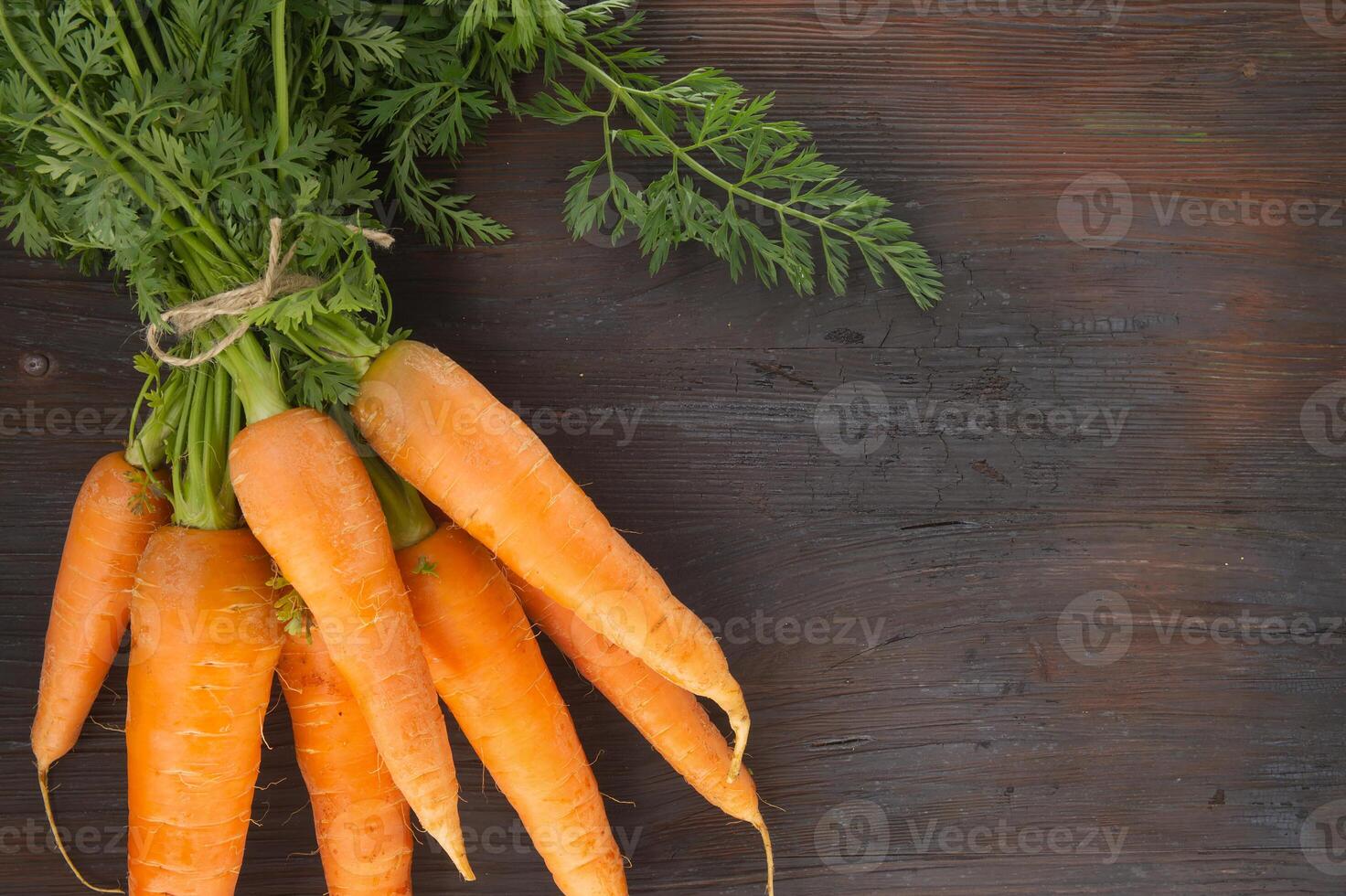 Bundle of fresh, orange carrots with green tops on wooden table photo