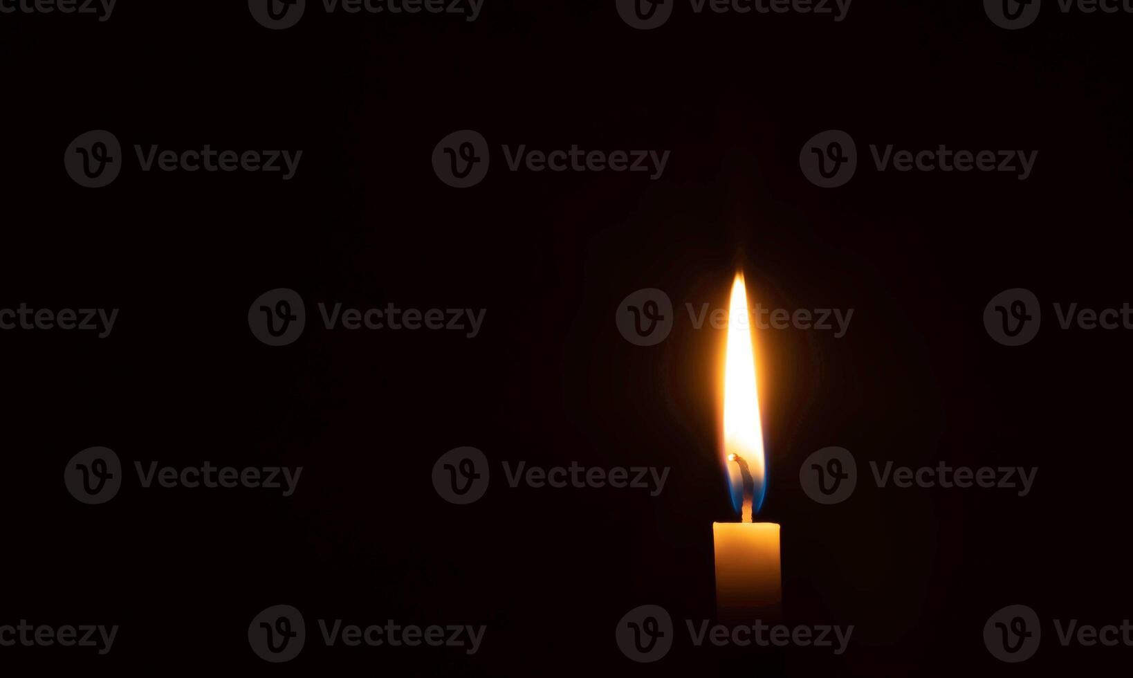 A single burning candle flame or light glowing on small orange candle on black or dark background on table in church for Christmas, funeral or memorial service with copy space photo