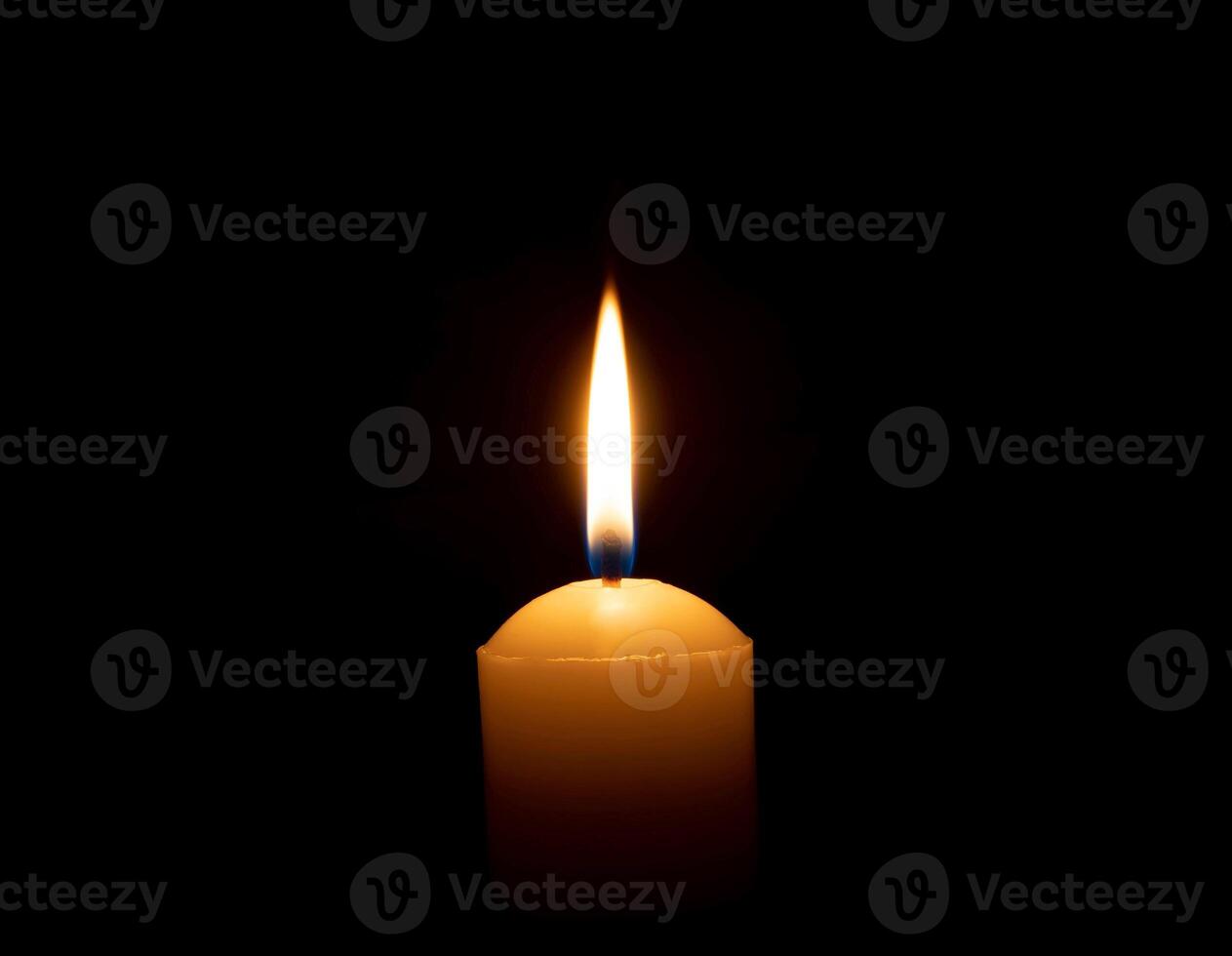 A single burning candle flame or light glowing on a big yellow candle on black or dark background on table in church for Christmas, funeral or memorial service with copy space photo