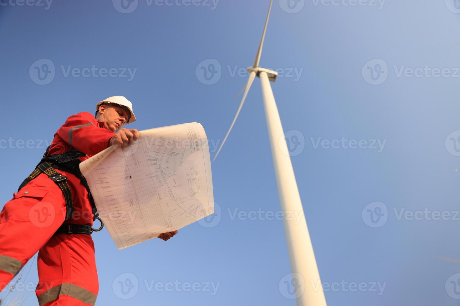 windmill engineer with red safety uniform hold drawing work at front of wind turbine farm photo
