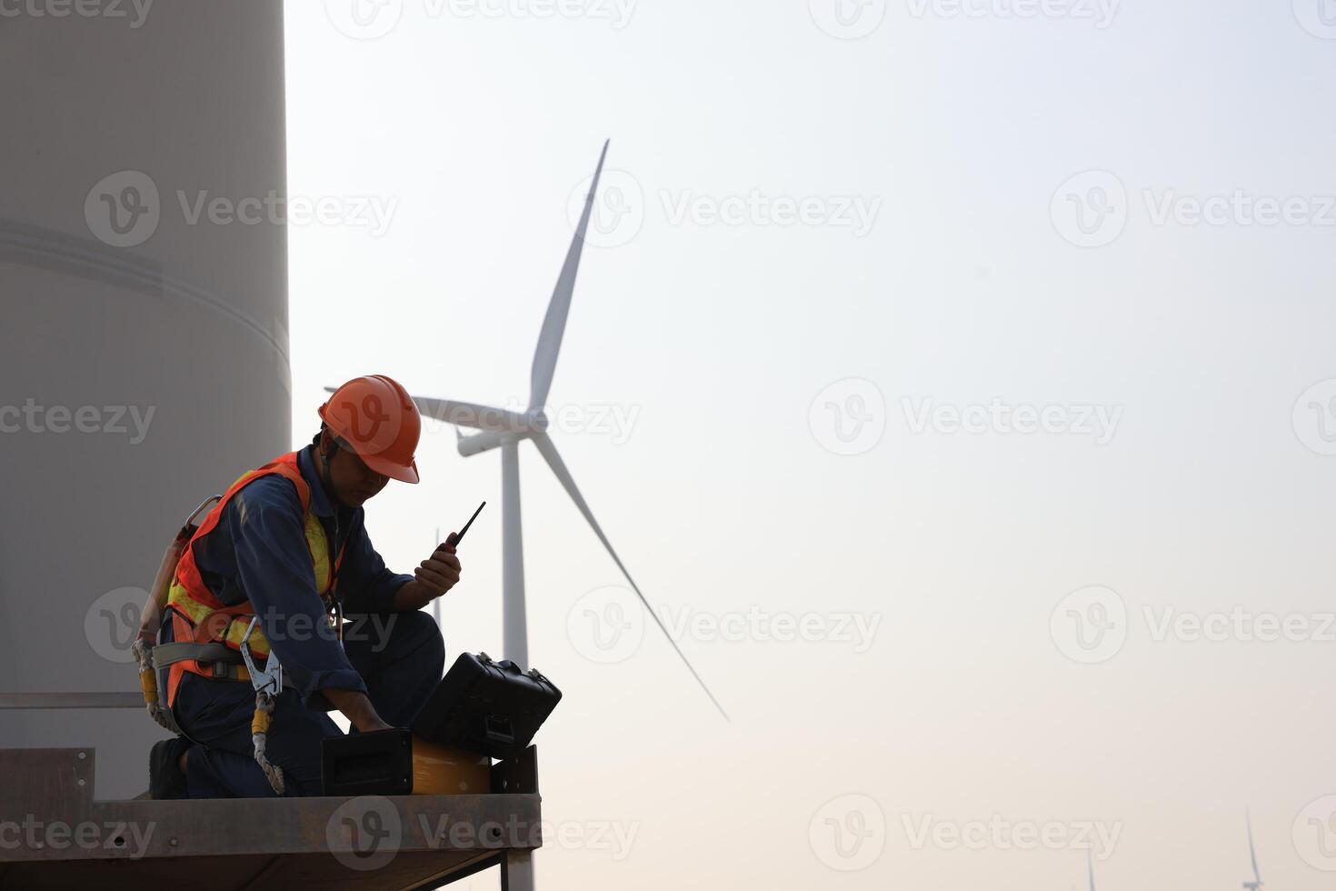 Specialist wind turbine technician working at the base of the turbine. Wind turbine service technician wearing safety uniform and safety harness working at windmill farm photo