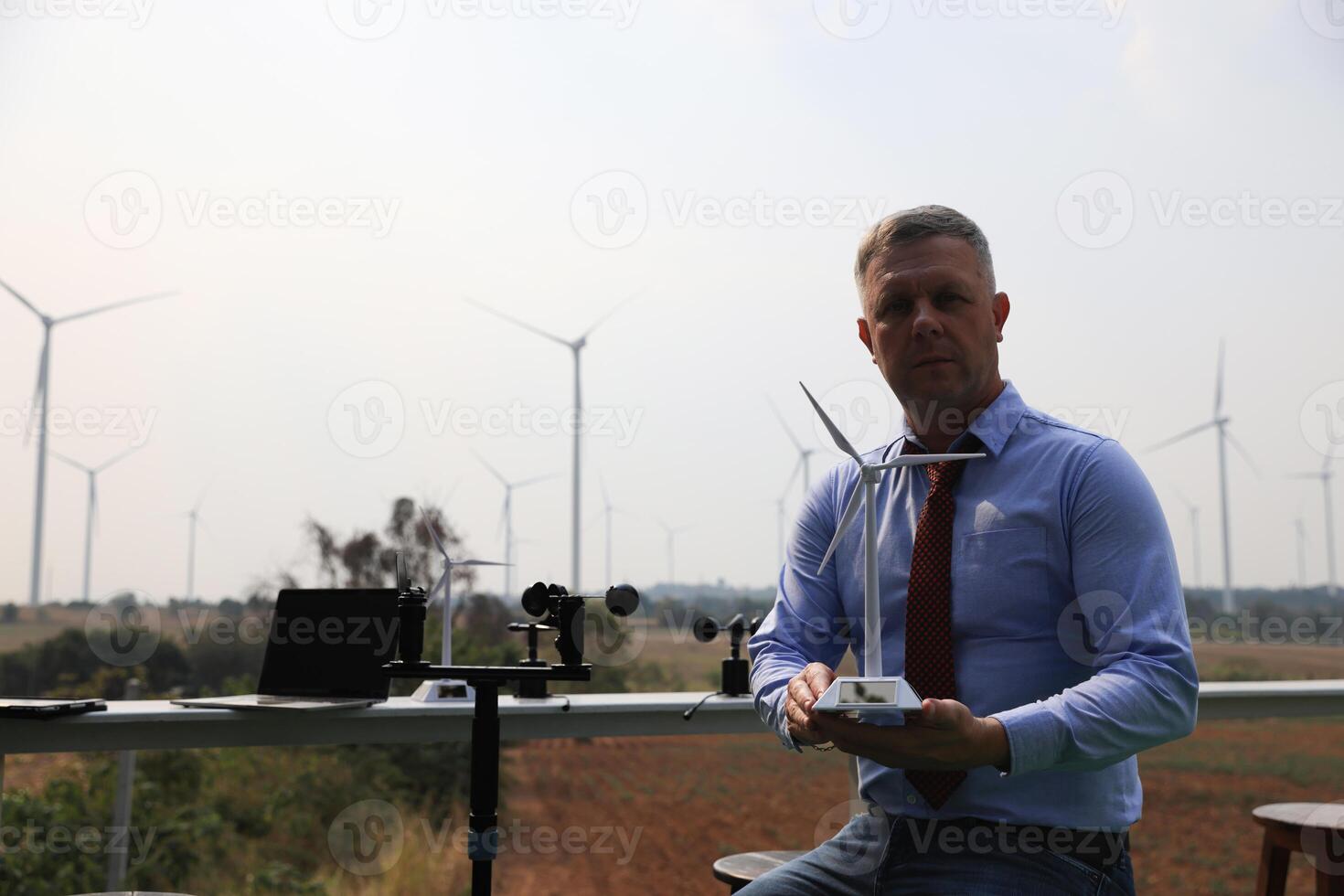 A senior male energy specialist is inspecting wind turbines on an ecological construction project using a wind speed measuring instrument at a windmill. photo