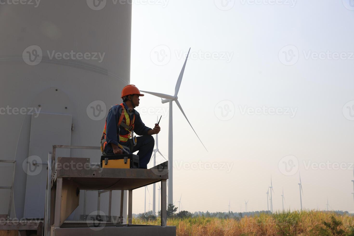 Specialist wind turbine technician working at the base of the turbine. Wind turbine service technician wearing safety uniform and safety harness working at windmill farm photo