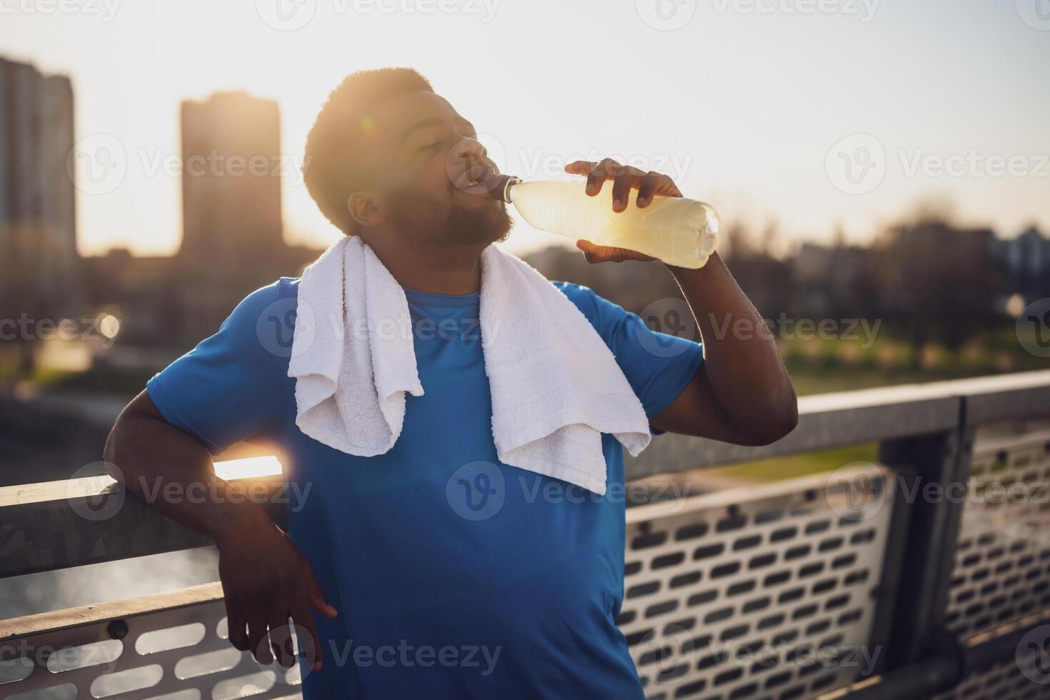 Portrait of young african-american man who is drinking water and relaxing after jogging. photo