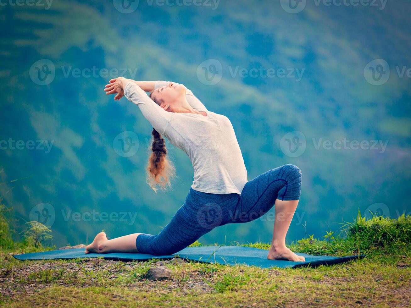 Sporty fit woman practices yoga asana Anjaneyasana in mountains photo
