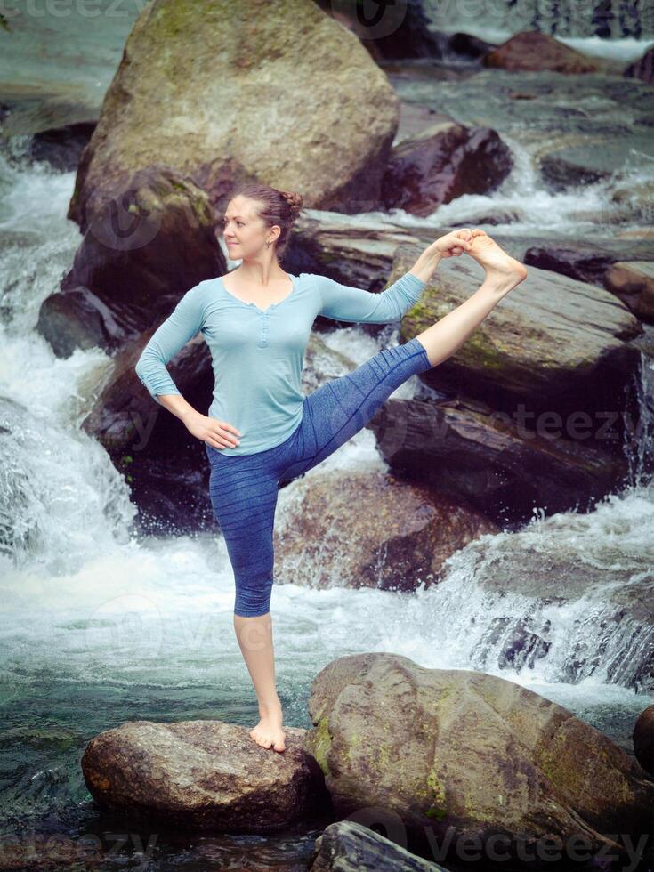Woman doing Ashtanga Vinyasa Yoga asana outdoors at waterfall photo
