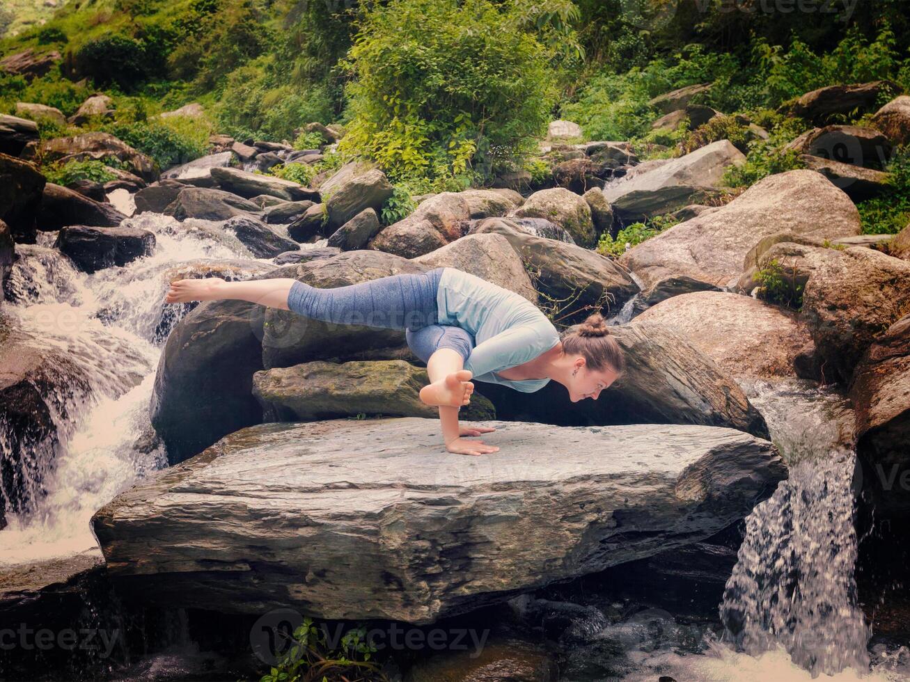 Young sporty fit woman doing yoga oudoors at tropical waterfall photo