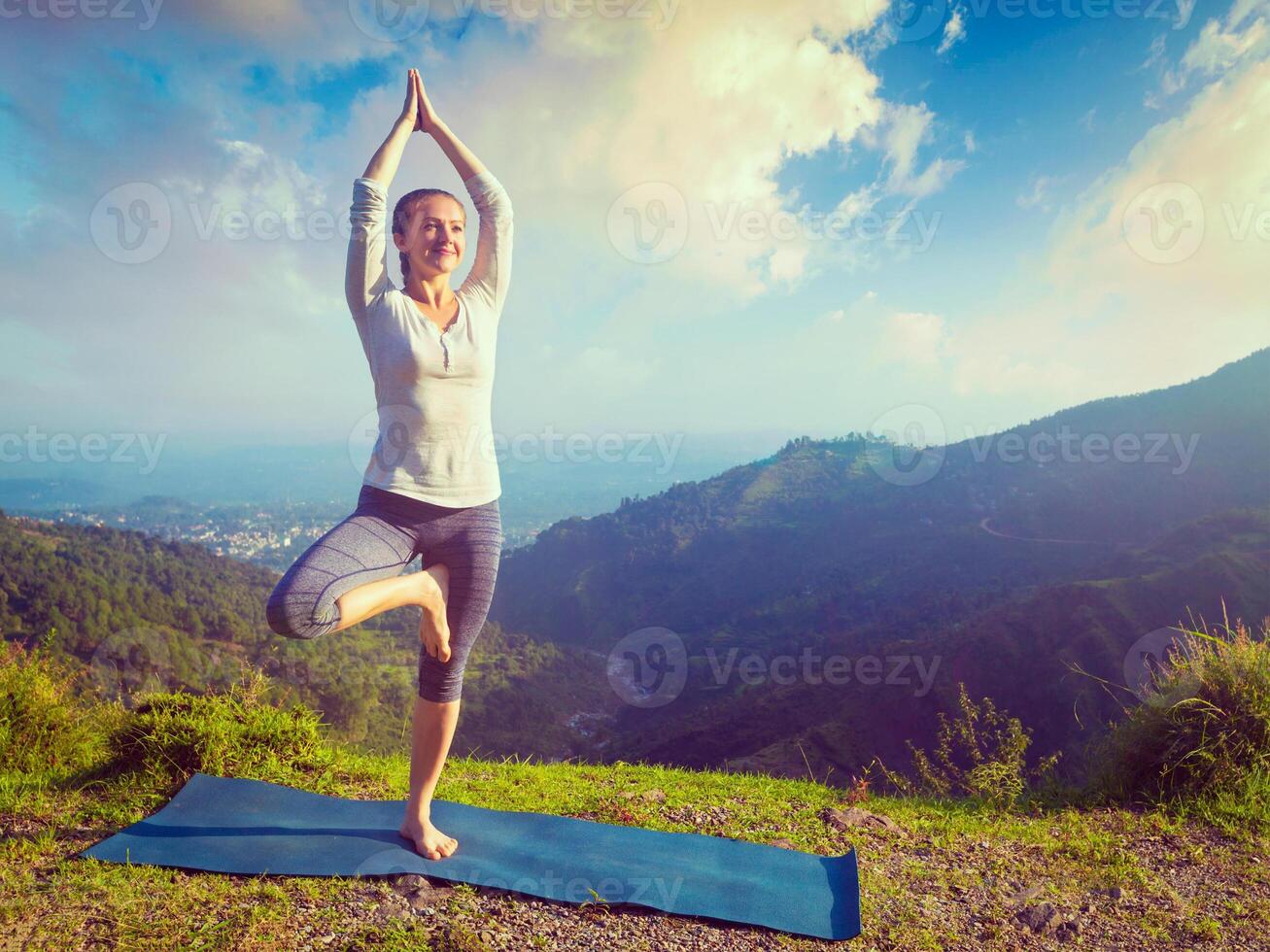 Woman in yoga asana Vrikshasana tree pose in mountains outdoors photo