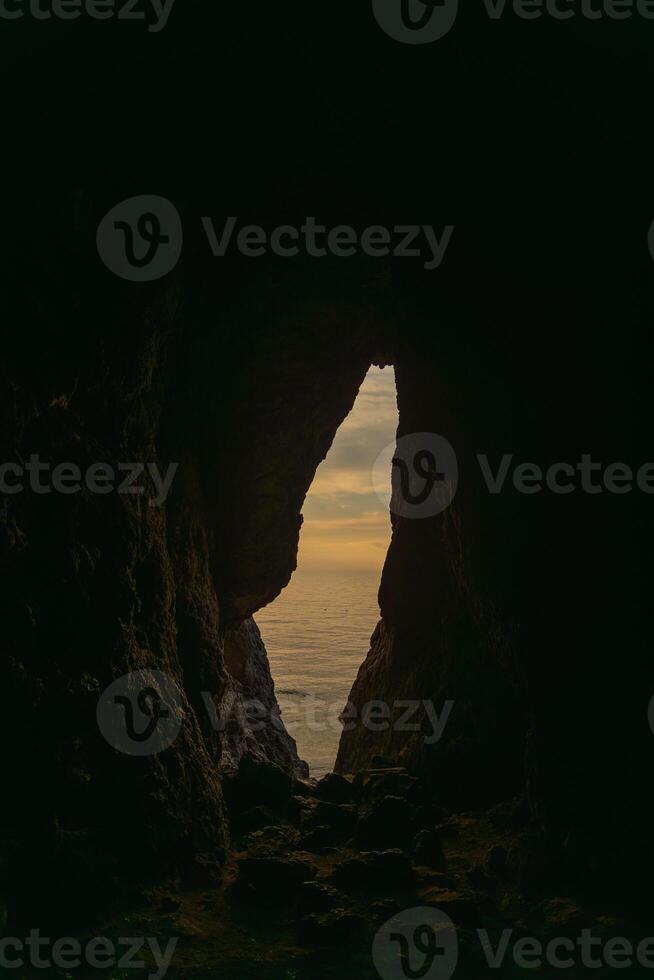 A cave with a small opening in the wall. The cave is dark and the sky is cloudy. photo