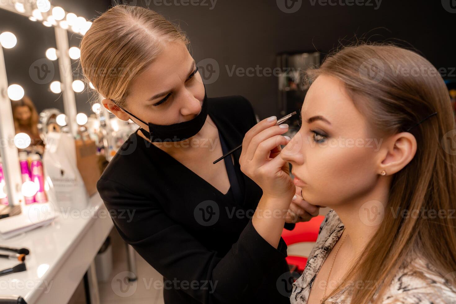 Make-up artist paints eyebrow pencil to beautiful brunette in be photo