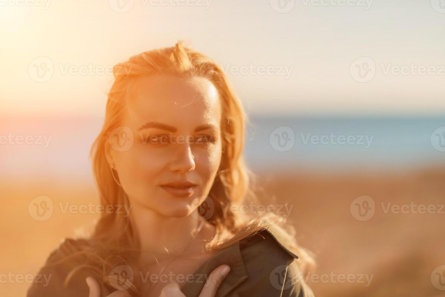 Portrait blonde sea cape. A calm young blonde in an unbuttoned khaki raincoat stands on the seashore, under the raincoat there is a black skirt and top photo