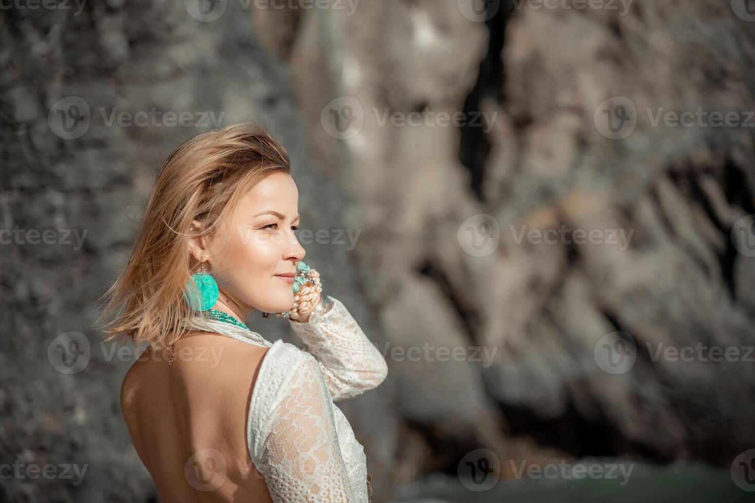 Middle aged woman looks good with blond hair, boho style in white long dress on the beach decorations on her neck and arms. photo