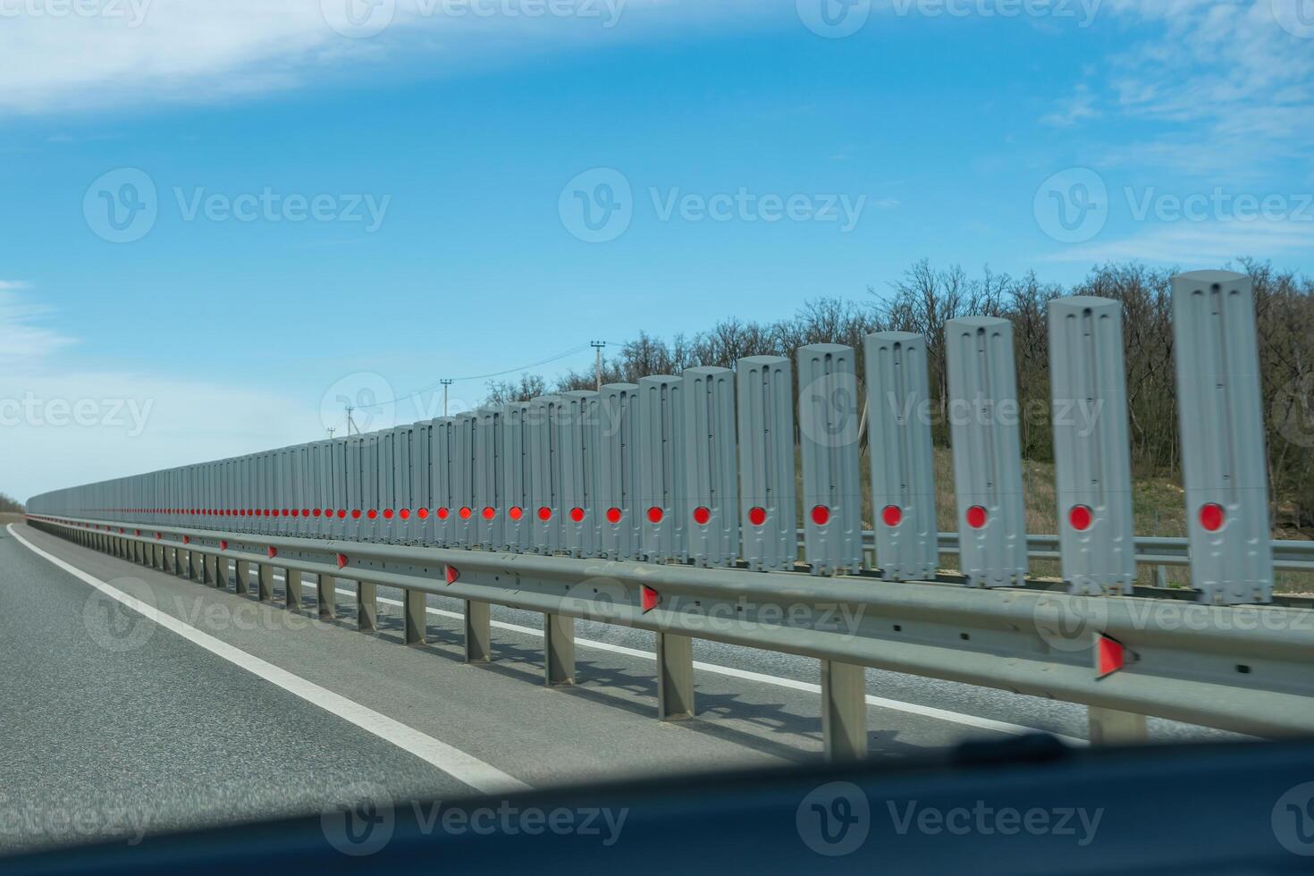 A road with a long line of metal posts with red hearts on them. The road is empty and the sky is clear. photo