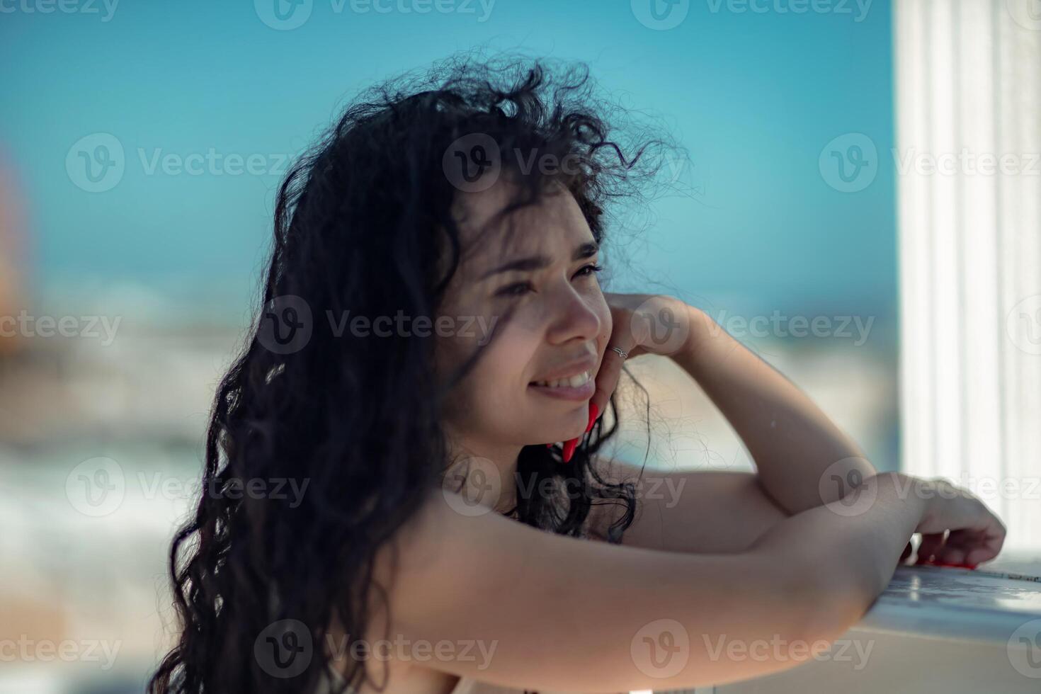 Sea woman rest. Portrait of a woman with long curly black hair in a beige dress stands on a balcony against the backdrop of the sea. Tourist trip to the sea. photo