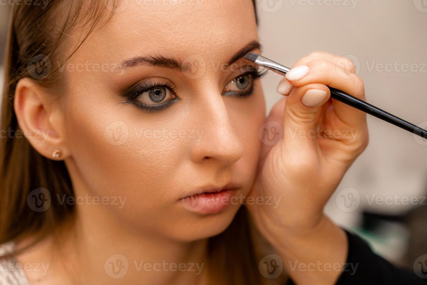 Make-up artist paints eyebrow pencil to beautiful brunette in be photo