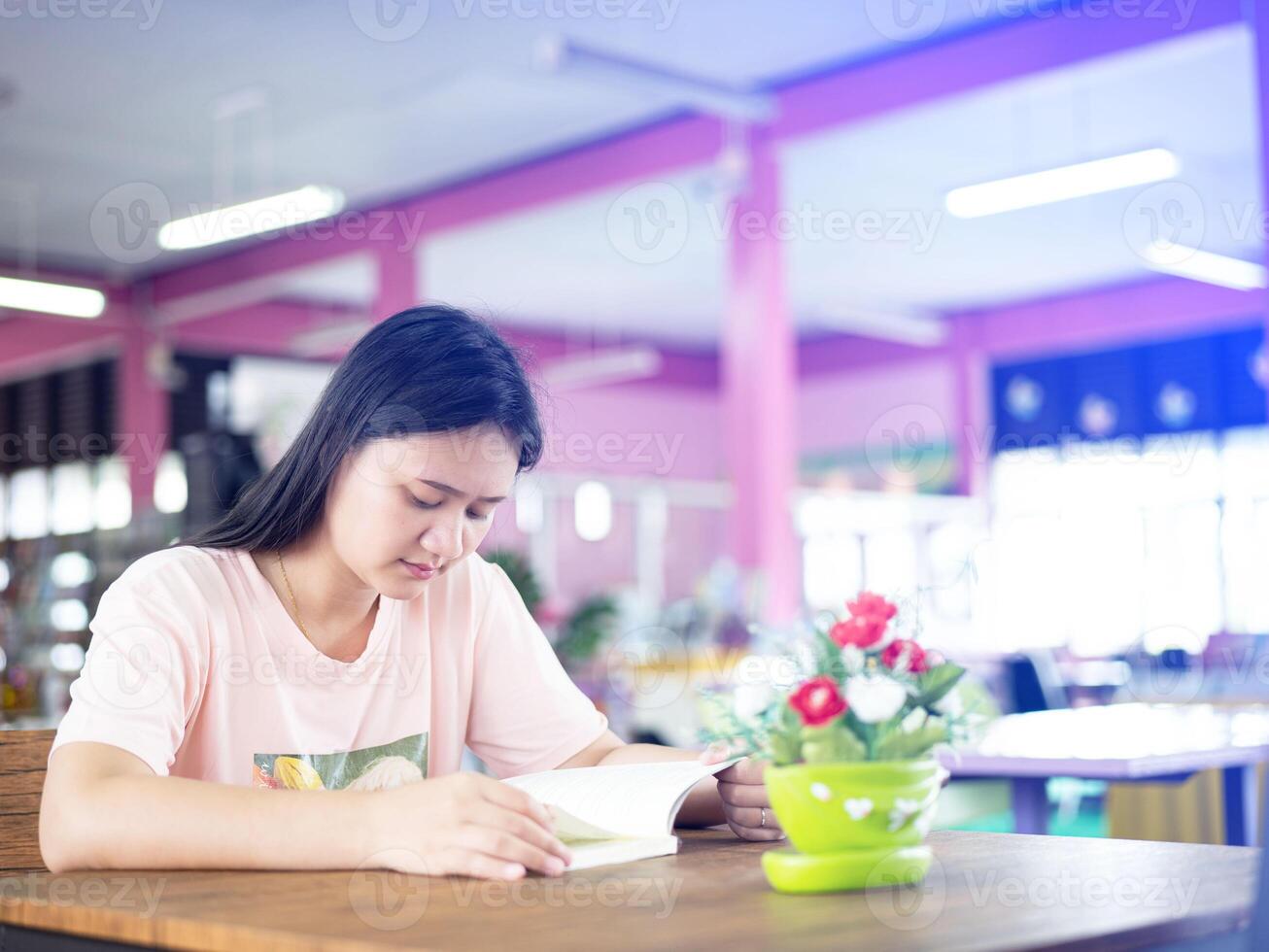 woman studying in the library  that full of books. Conception of education.in modern interior library of university choosing book between bookshelves at library. sitting on the table reading a book photo