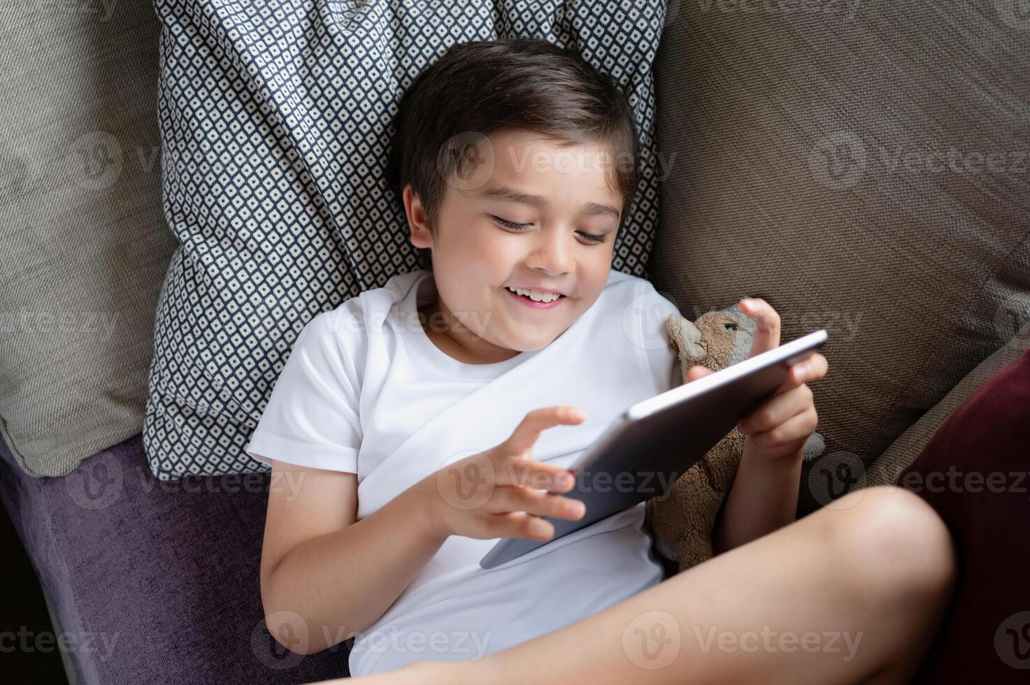 Kid doing homework with digital tablet in living room,Child using gadgets to study.School boylearns online from home,Education learning with new technology for kids. photo