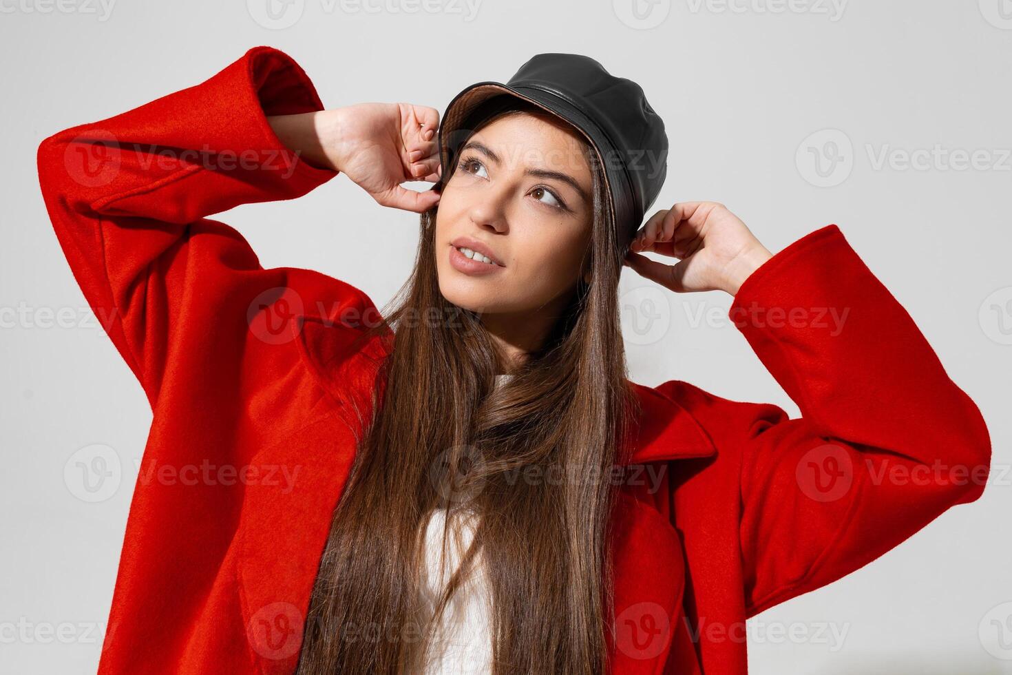 Trendy winter accsesorises. Pretty girl in black hat and red coat  raised hands and holding cap in studio on white background. photo