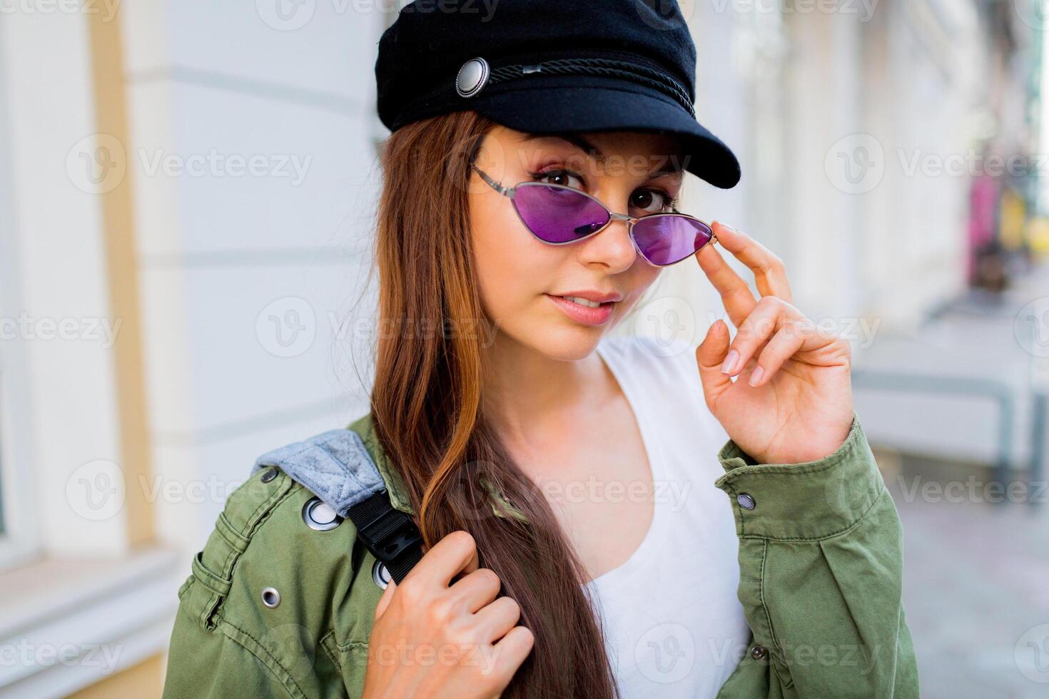 Happy brunette weoman posing outdoor . Stylish hat, sunglasses and green jacket. photo