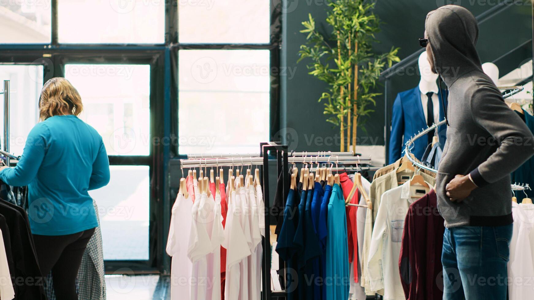 African american thief stole stylish clothes in clothing store, being caught by asian security guard. Robber running from bodyguard, trying to escape the crime accusations. Robbery concept photo