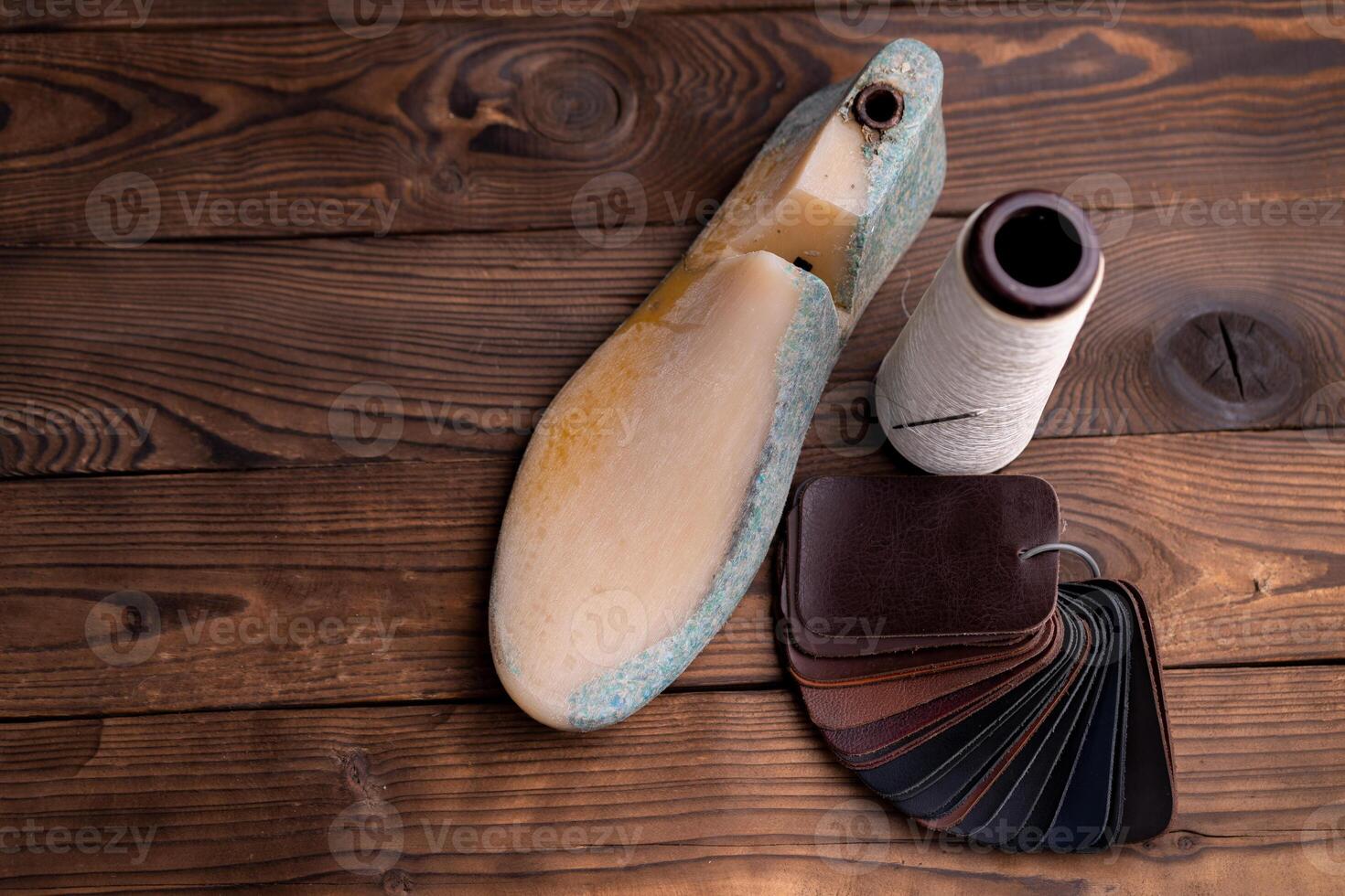 Leather samples for shoes and wooden shoe last on dark wooden table. photo