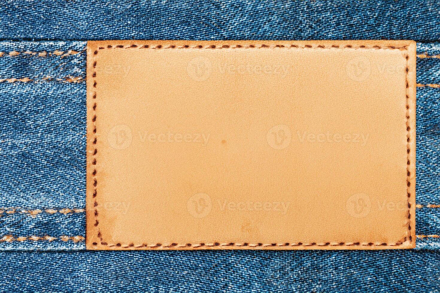 A fashion-themed backdrop featuring a vacant area for graphic design purposes. An unoccupied leather label tag is present. The texture of blue jeans denim is visible, complete with sewn thread lines. photo