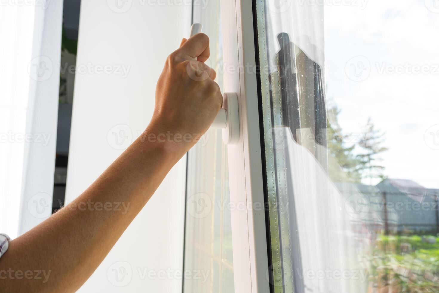 The hand holds the handle of a plastic double-glazed window, closing and opening the window with a rotary mechanism, the position of the handle for ventilation, micro-ventilation photo