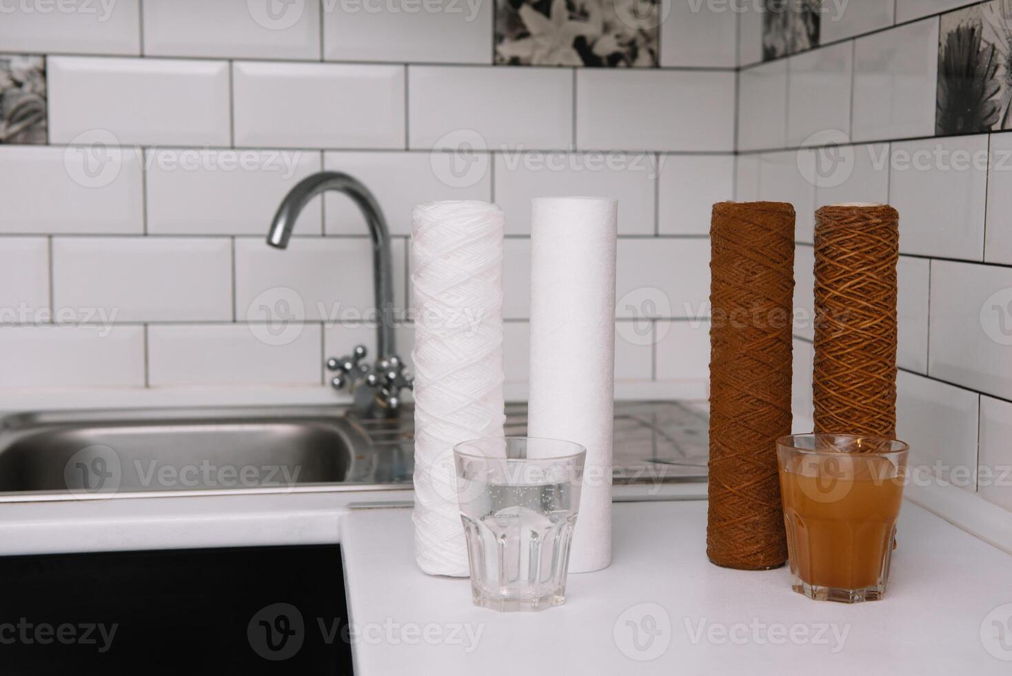 Water filter cartridge used and a glass of rusty water brown coloring and new filter and a glass of clean water. Evidence of contamination of tap water with iron cations. white kitchen photo