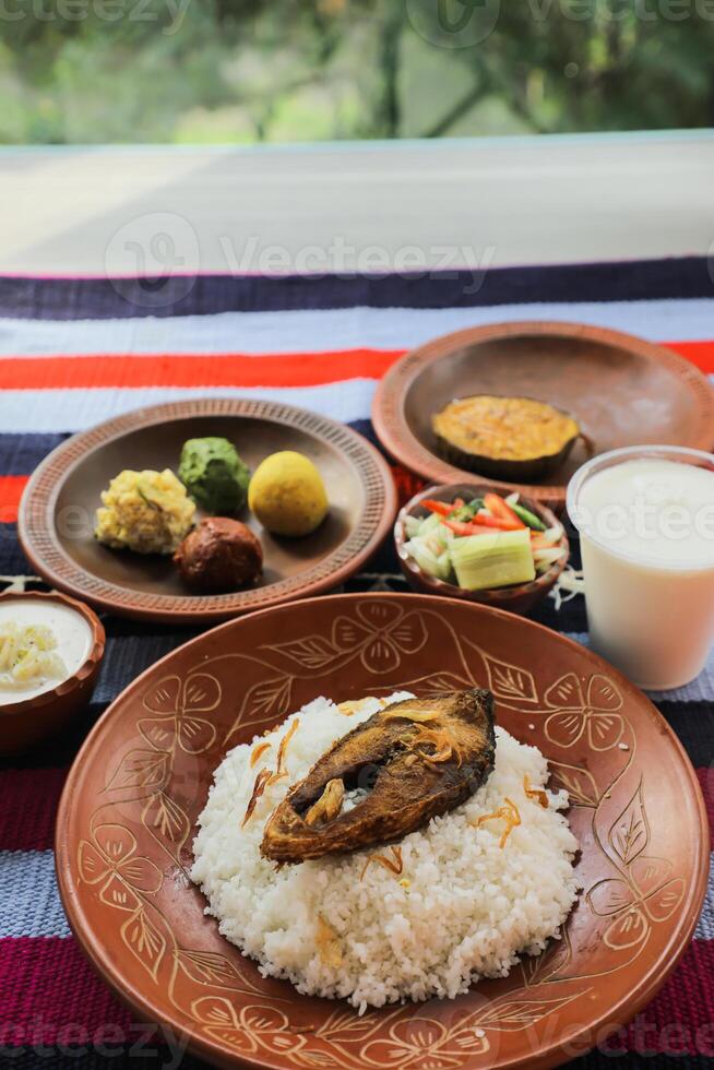Khuder Bhat, Hilsa Khichuri Combo with salad, eggplant, borhani and Chui Pitha served in dish isolated on mat top view of indian and bangladeshi food photo