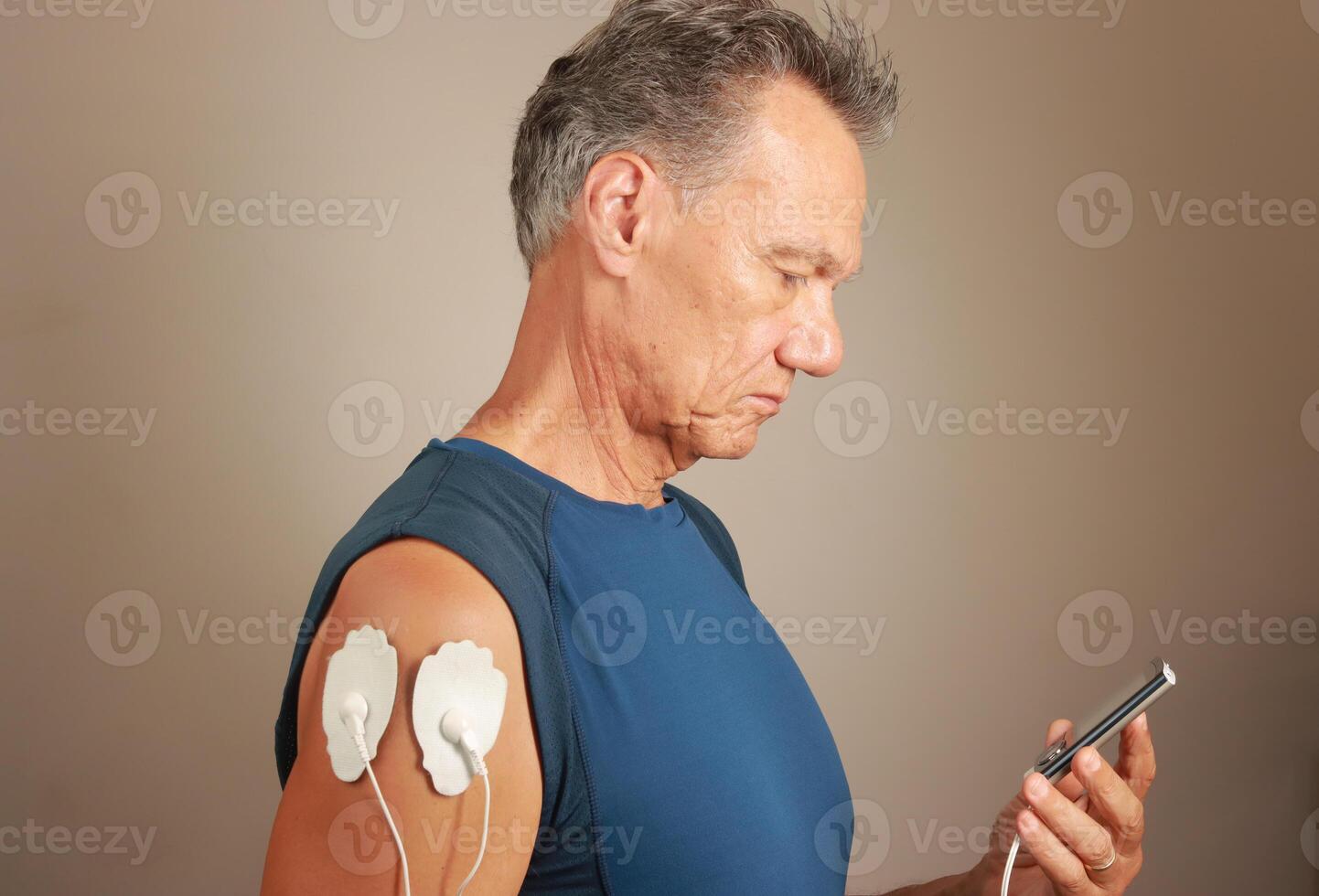 Man using an Electro Therapy Massager or Tens Unit on his Deltoids for pain relief for Muscles and Joints photo