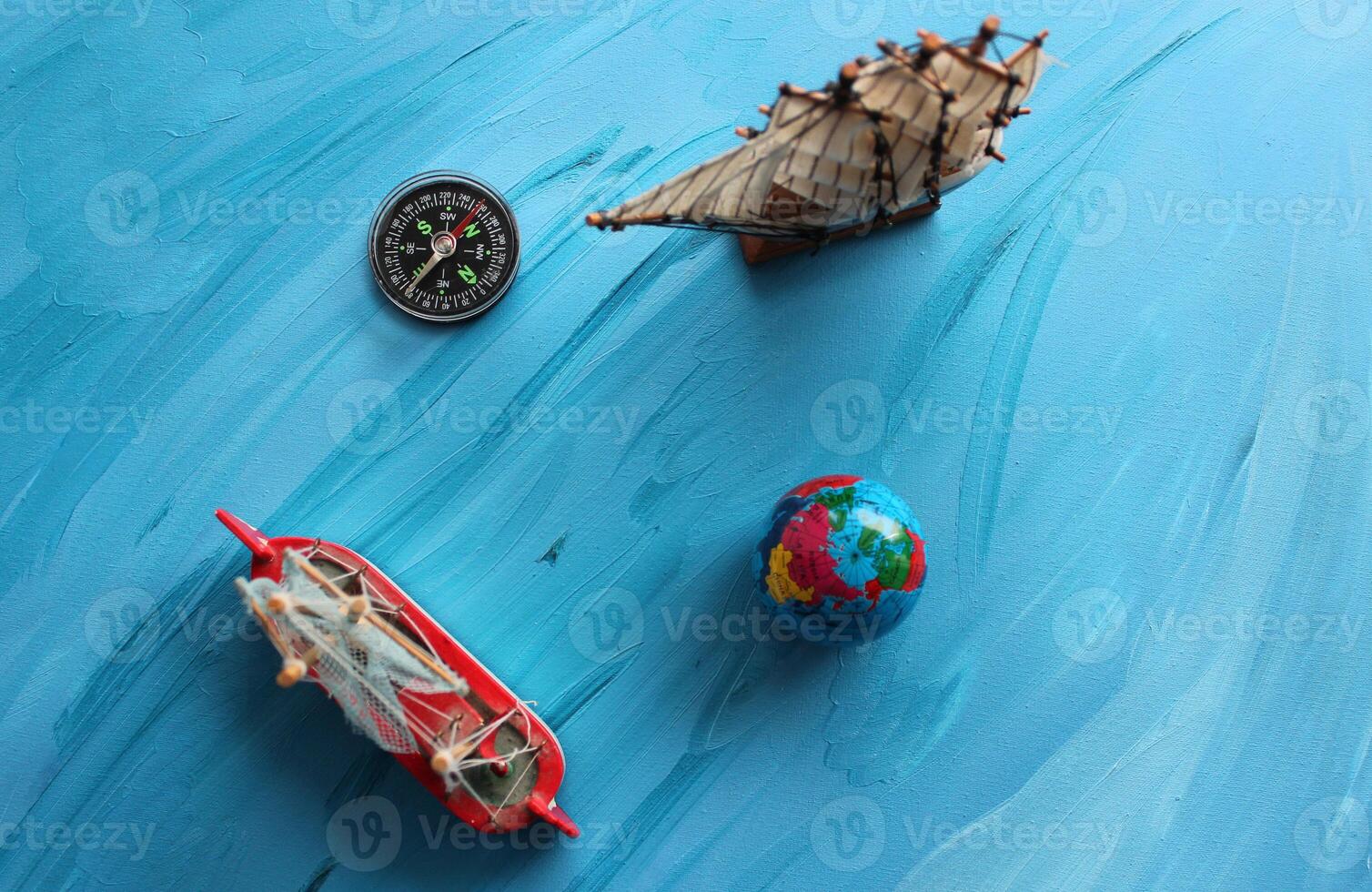 Miniatures on the theme of sea travel. Compass And Small Globe Near Sailing Ships Model On Blue Painted Surface photo