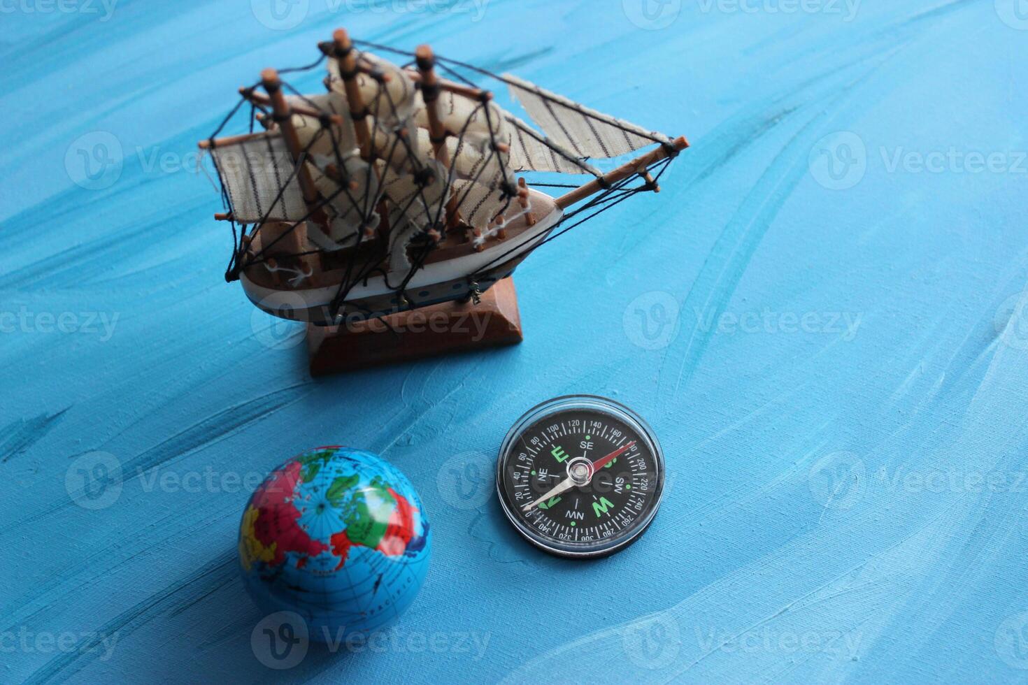 Circle Compass With Blurred Masted Ship Model And Small Globe Around On Blue Surface With Painted Waves photo