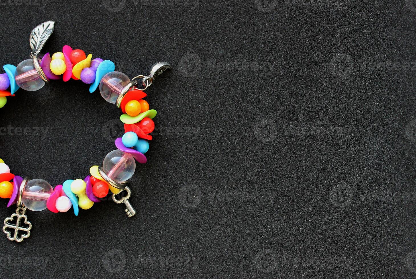 Concept For Postcard Or Invitation. Bracelet With Colorful Beads And Silver Charms In A Side Of Image On Black Background photo