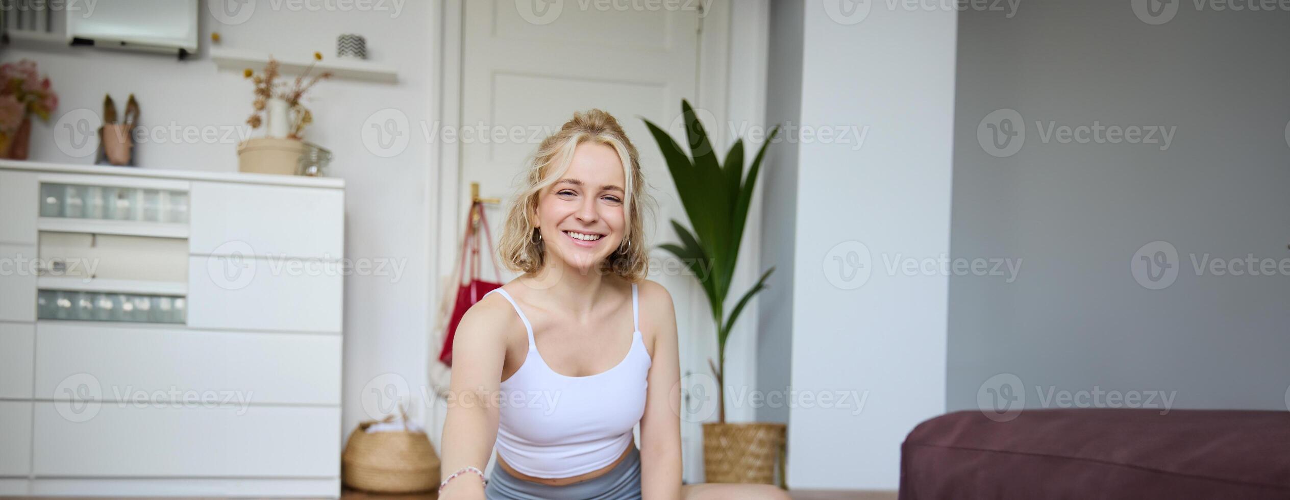 Vertical shot of smiling young woman, content creator using digital camera during workout, shooting a vlog about fitness training and home exercises, recording her yoga photo