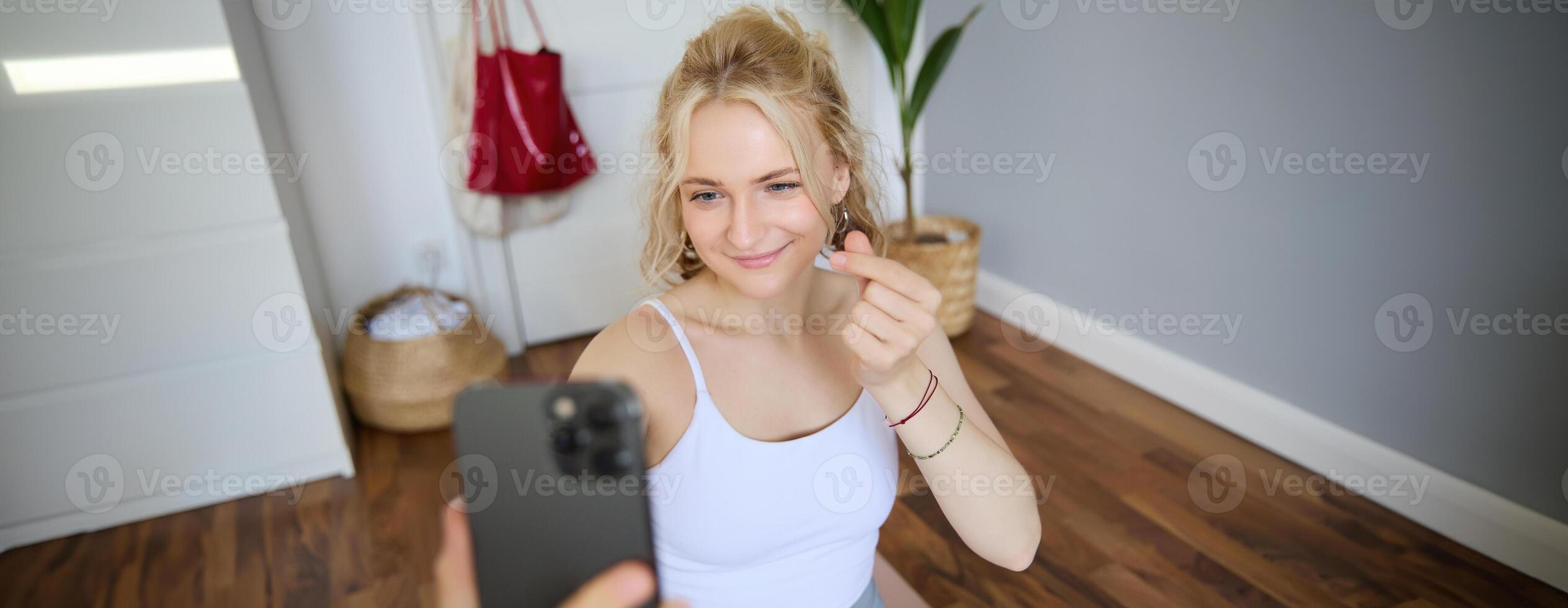 Portrait of smiling, beautiful young woman, social media content creator, takes selfies on smartphone during workout, doing exercises at home on yoga mat photo