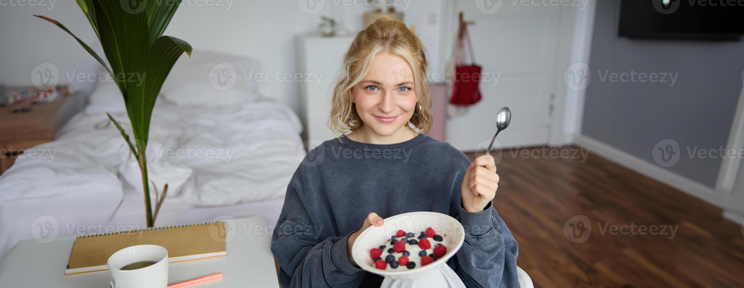 Portrait of young vlogger, content creator, showing her homemade breakfast on camera, eating dessert, smiling and looking happy photo