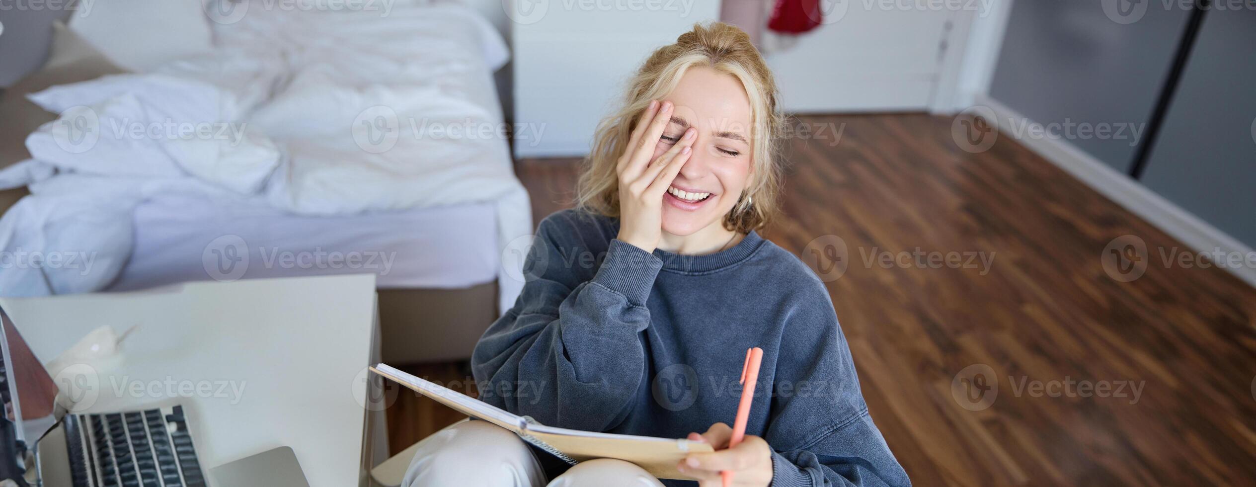 Portrait of charismatic blond girl, smiling woman in bedroom, holding notebook and pen, writing in journal or diary, creates to do list in planner photo