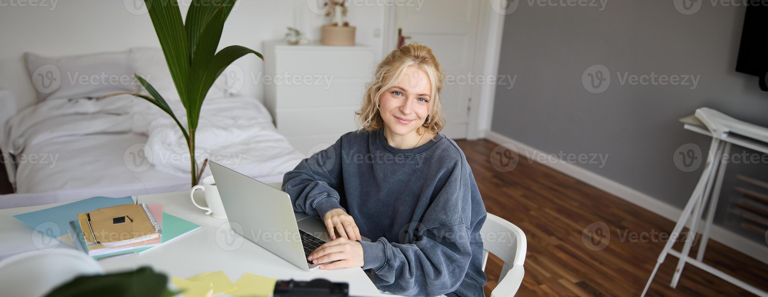 Portrait of young blond woman with laptop, recording on digital camera, created blog, vlogging in her room, editing on computer photo