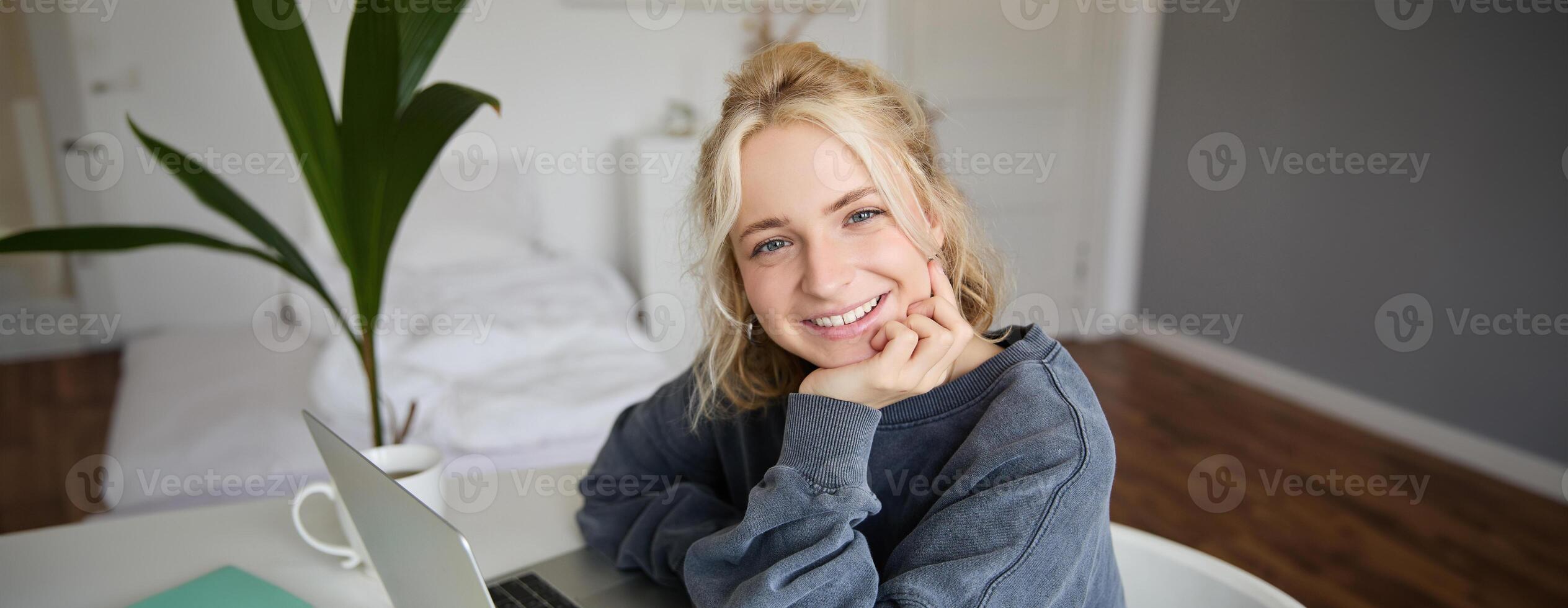 Close up portrait of young smiling female model, sits in a room with laptop, works from home, does online course, e-learning photo