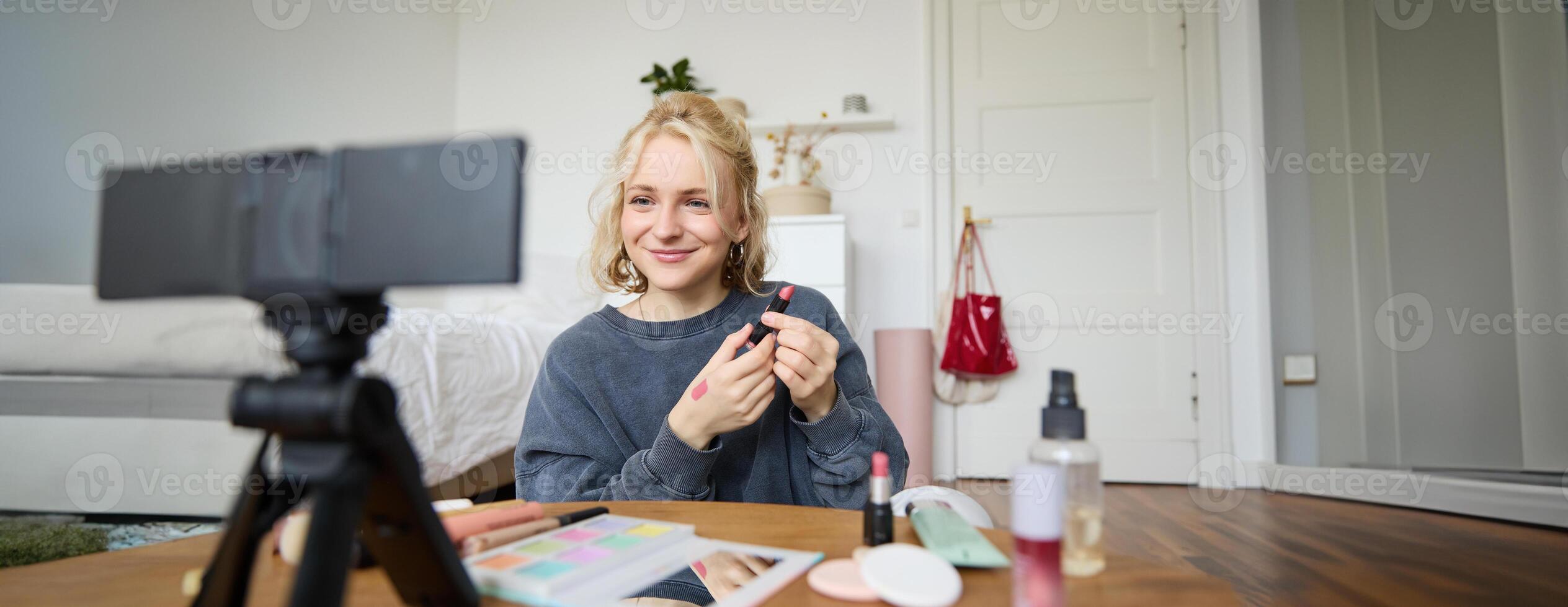Portrait of young content maker, woman blogger recording a on digital camera, showing lipstick colour to her followers, creating lifestyle vlog for social media account photo