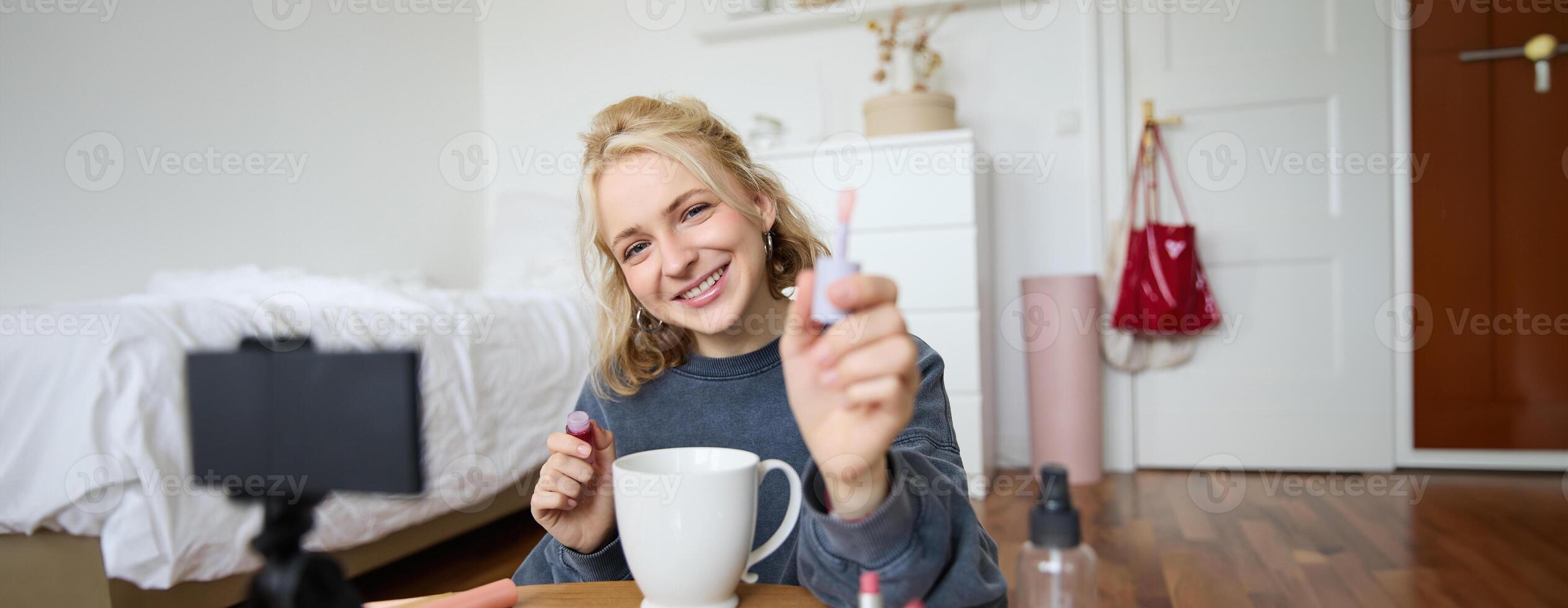 Portrait of smiling woman shows lip gloss, advertising makeup on her social media account, recording on digital camera, content maker working on new project in her room photo
