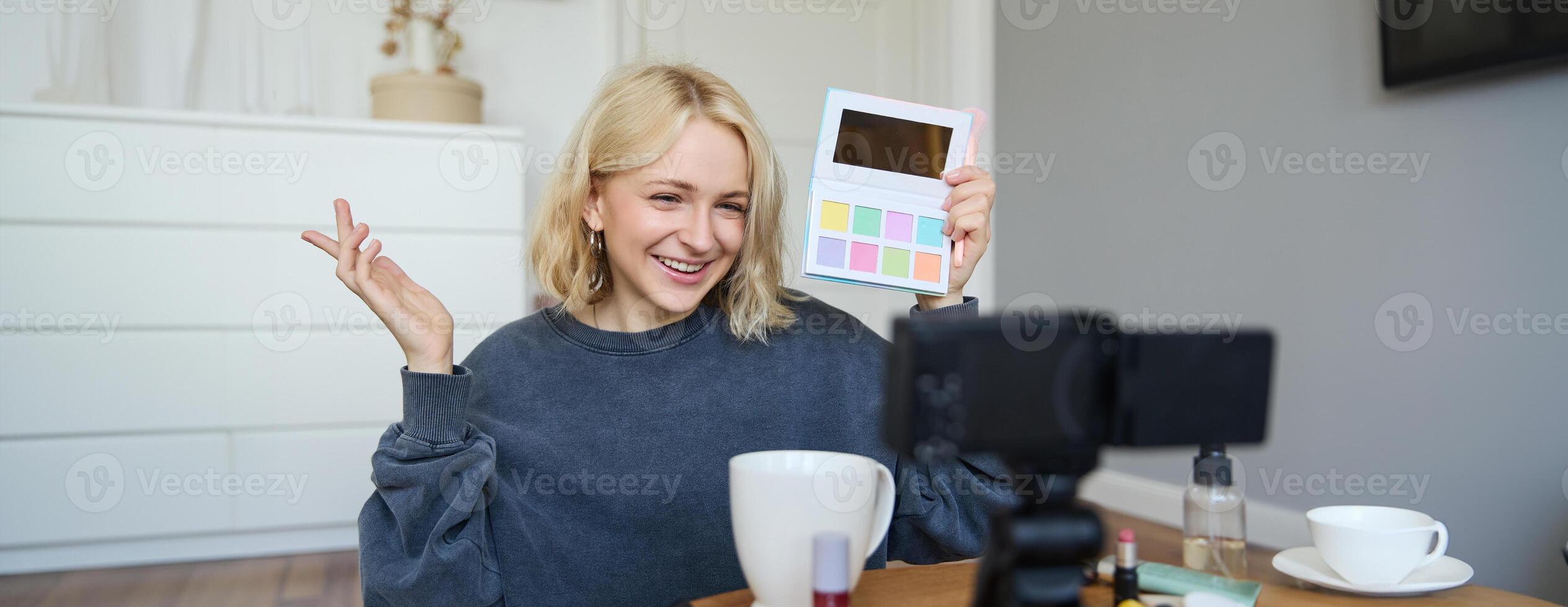 Portrait of beautiful lifestyle blogger, girl records a on her camera for social media, shows palette of eyeshadows, does a makeup tutorial for her followers, sits in her room photo