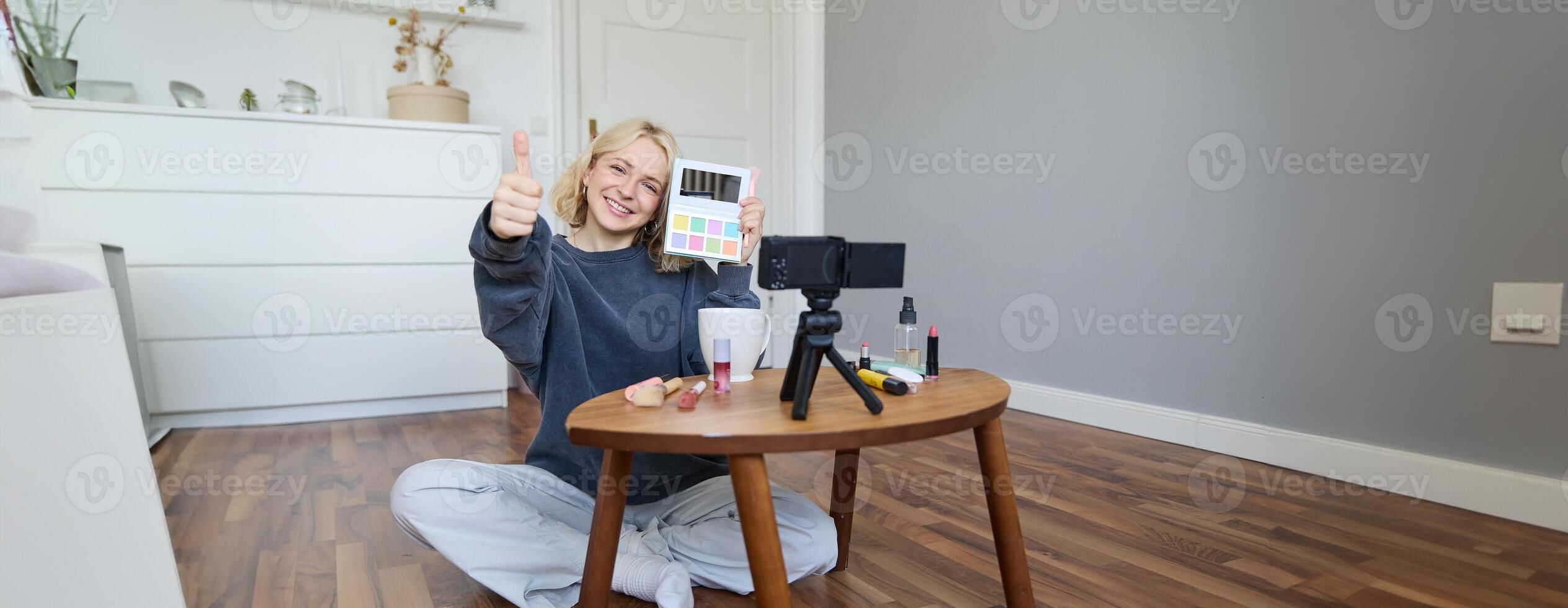 Portrait of beautiful smiling woman, recording in her room, has camera on coffee table, reviewing makeup, doing lifestyle vlog for social media account, records a tutorial photo