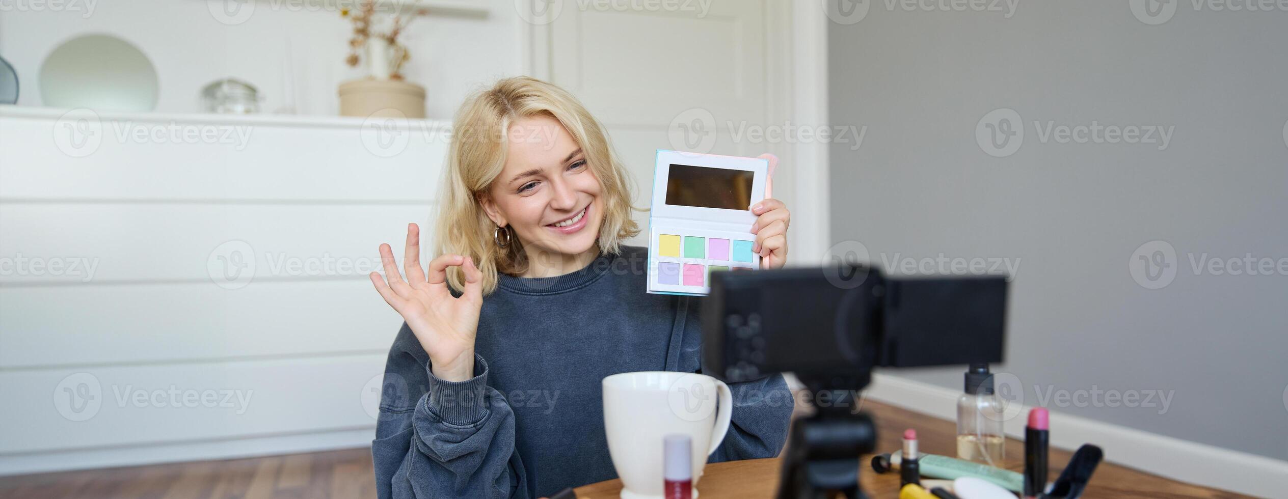 Portrait of beautiful smiling woman, recording in her room, has camera on coffee table, reviewing makeup, doing lifestyle vlog for social media account, records a tutorial photo
