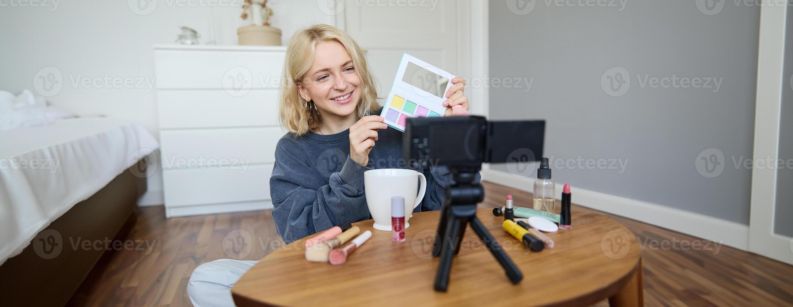 Portrait of beautiful smiling woman, recording in her room, has camera on coffee table, reviewing makeup, doing lifestyle vlog for social media account, records a tutorial photo